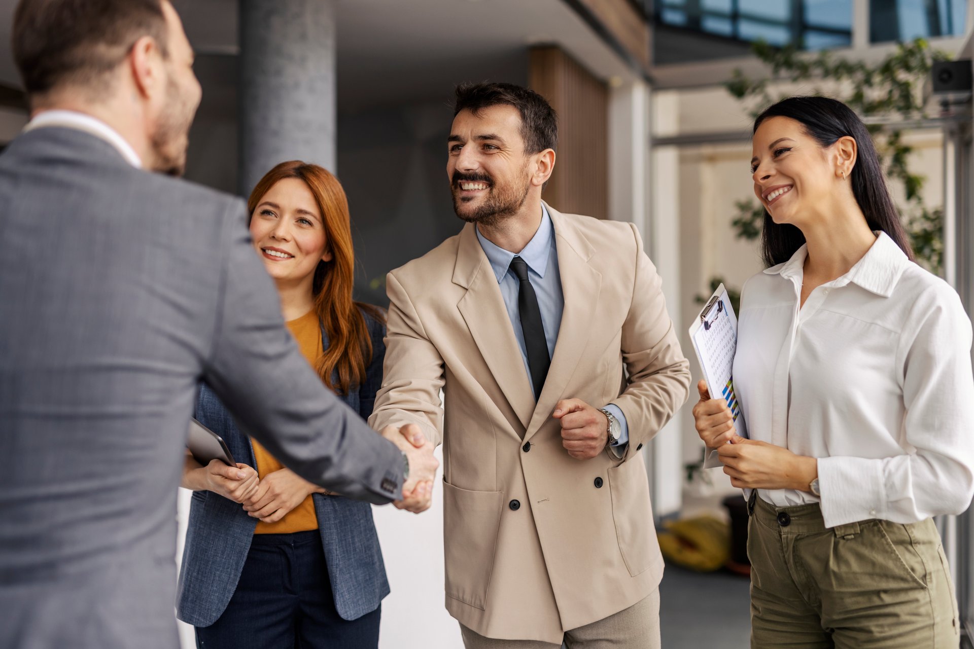Businessmen shaking hands and greeting while female managers standing and smiling at them.