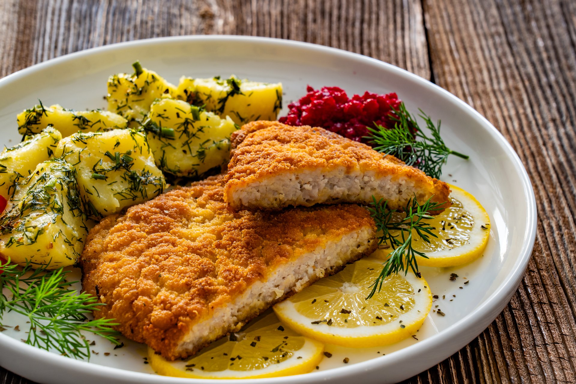 Crispy breaded fried pork chop, boiled potatoes and fresh vegetables served on wooden table