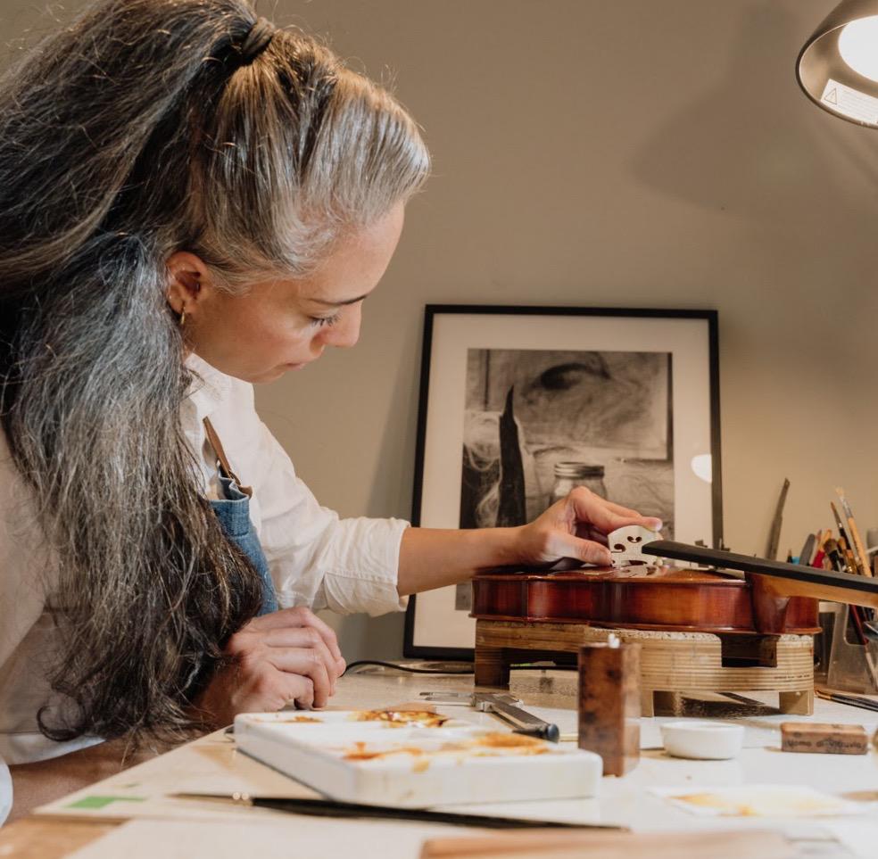 Luthier examining a partially constructed violin in a workshop setting, carefully inspecting the craftsmanship and structural integrity of the wooden instrument during the meticulous building process.