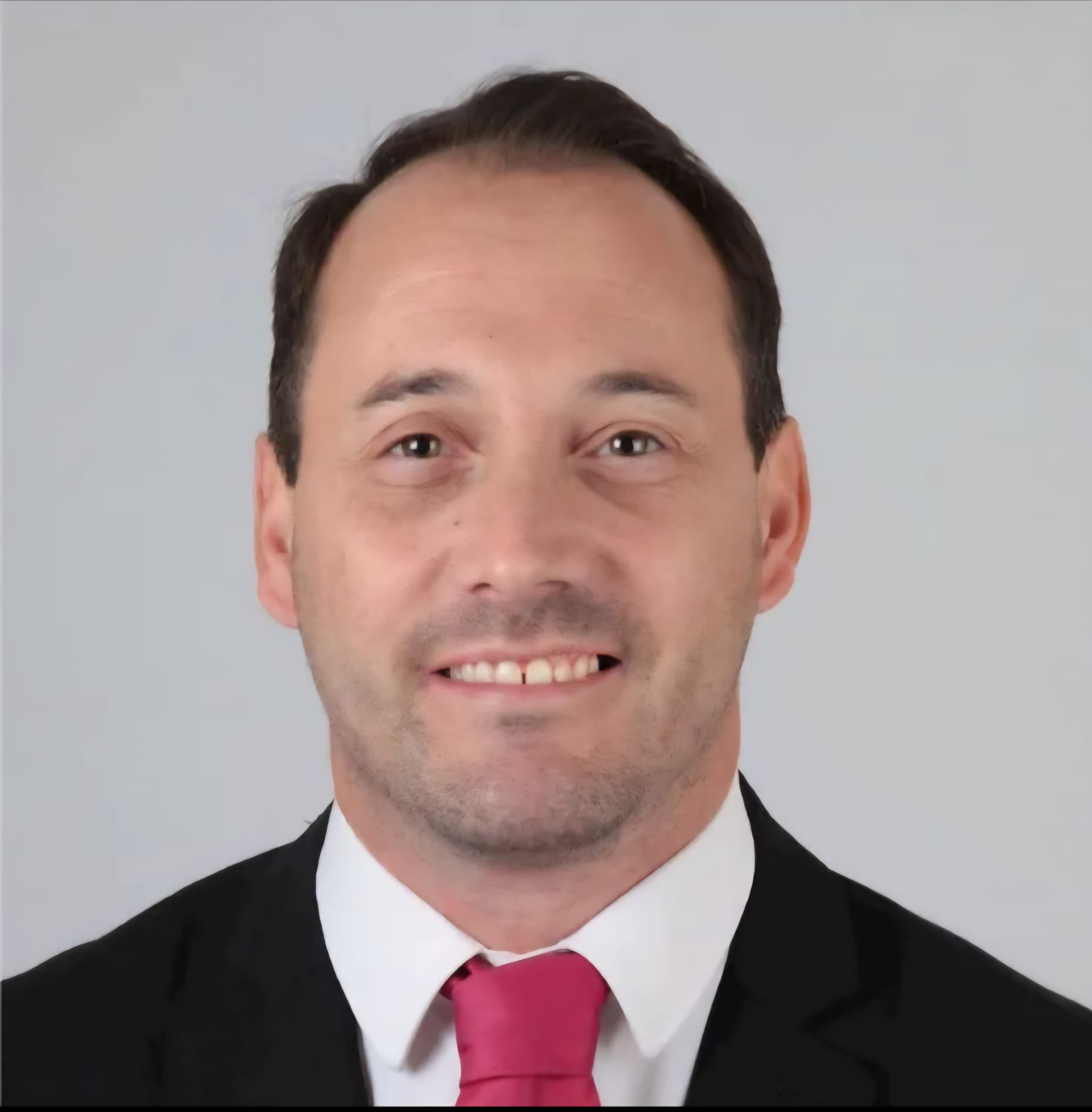 Smiling man in a suit and red tie, posing against a plain background.