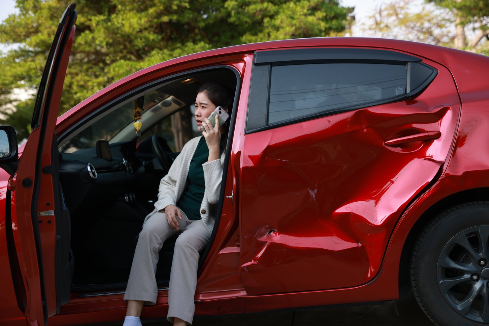 A female motorist is standing on the side of the road after a car accident, assessing the damage to her vehicle. She confidently calls for roadside assistance, detailing her location and the nature of the incident. Her insurance information is readily available, ensuring a smooth interaction with the service provider as she seeks help getting back on the road.
