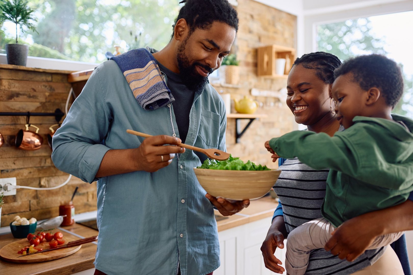 Happy African American man and his family preparing salad in the kitchen