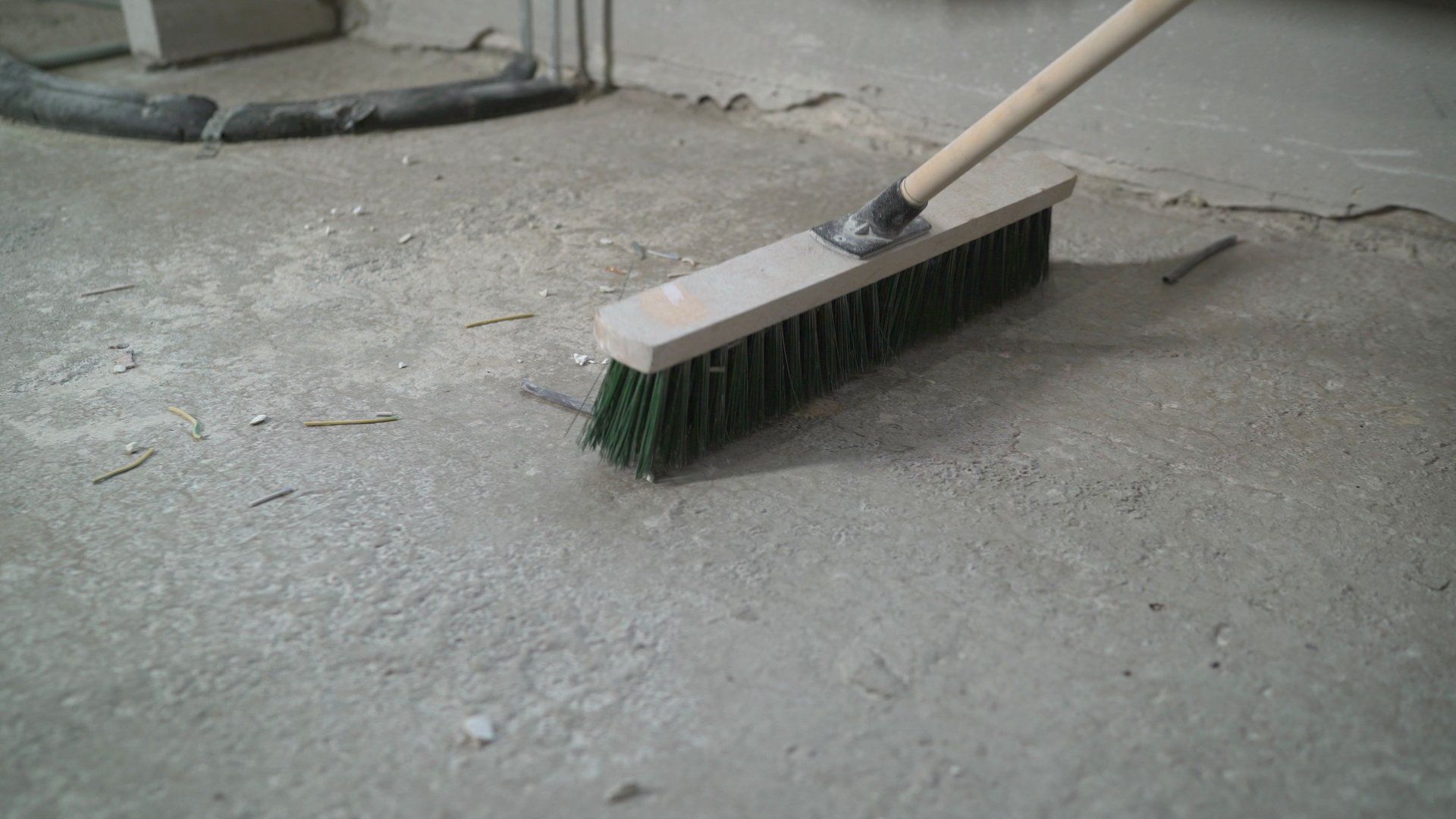 Preparing the floor for cover. The hand of a working man holds a broom, sweeping the concrete floor. A worker is cleaning a concrete floor.