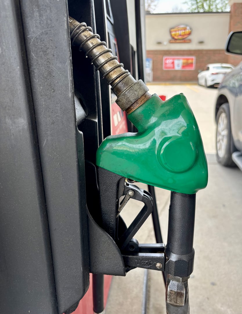 A green gas pump with a vehicle in background.