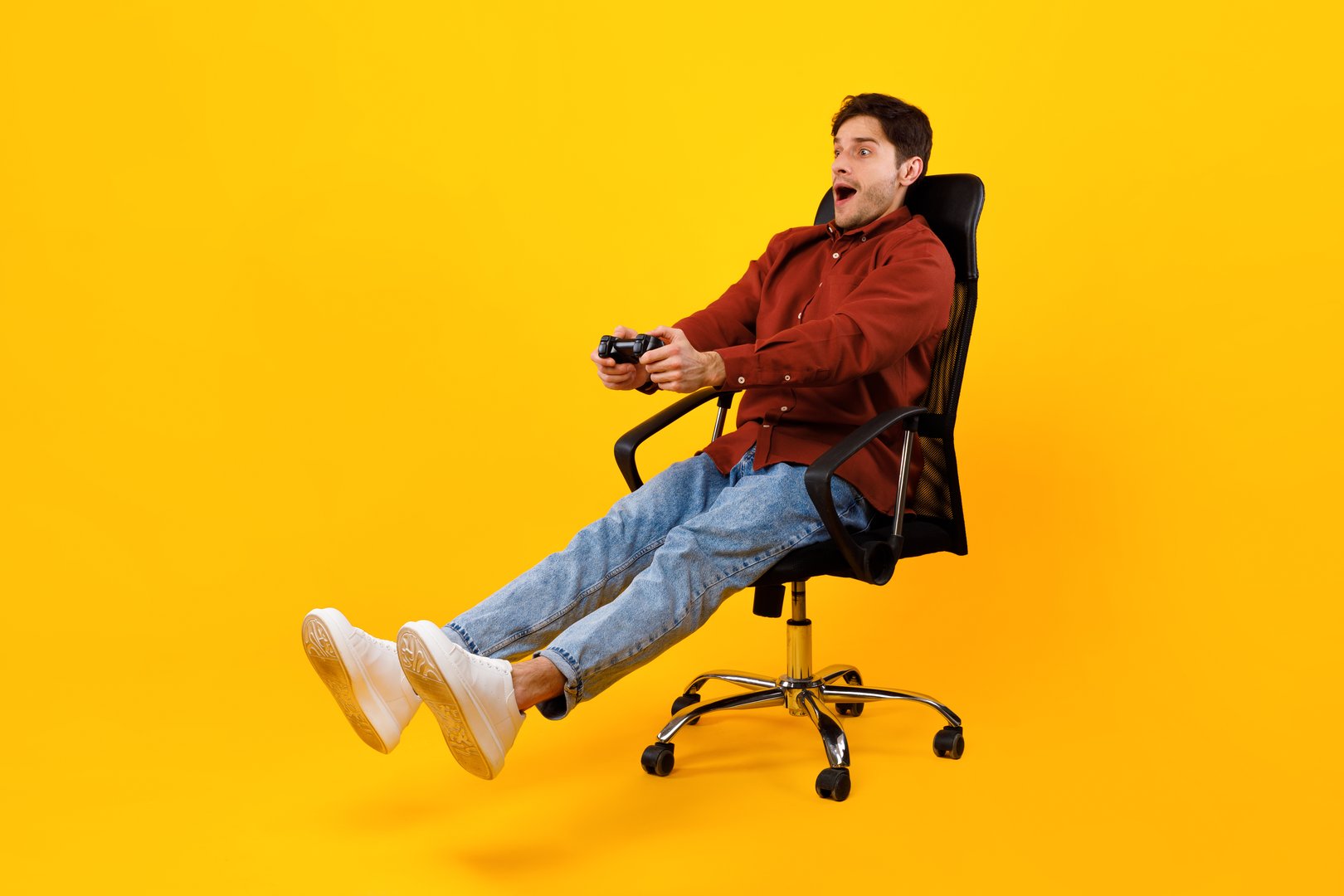 Excited Gamer Guy Playing Video Game Shouting Holding Gamepad Controller Looking Aside In Excitement Sitting In Chair Over Yellow Studio Background. Technology, Entertainment And Mobile Gaming