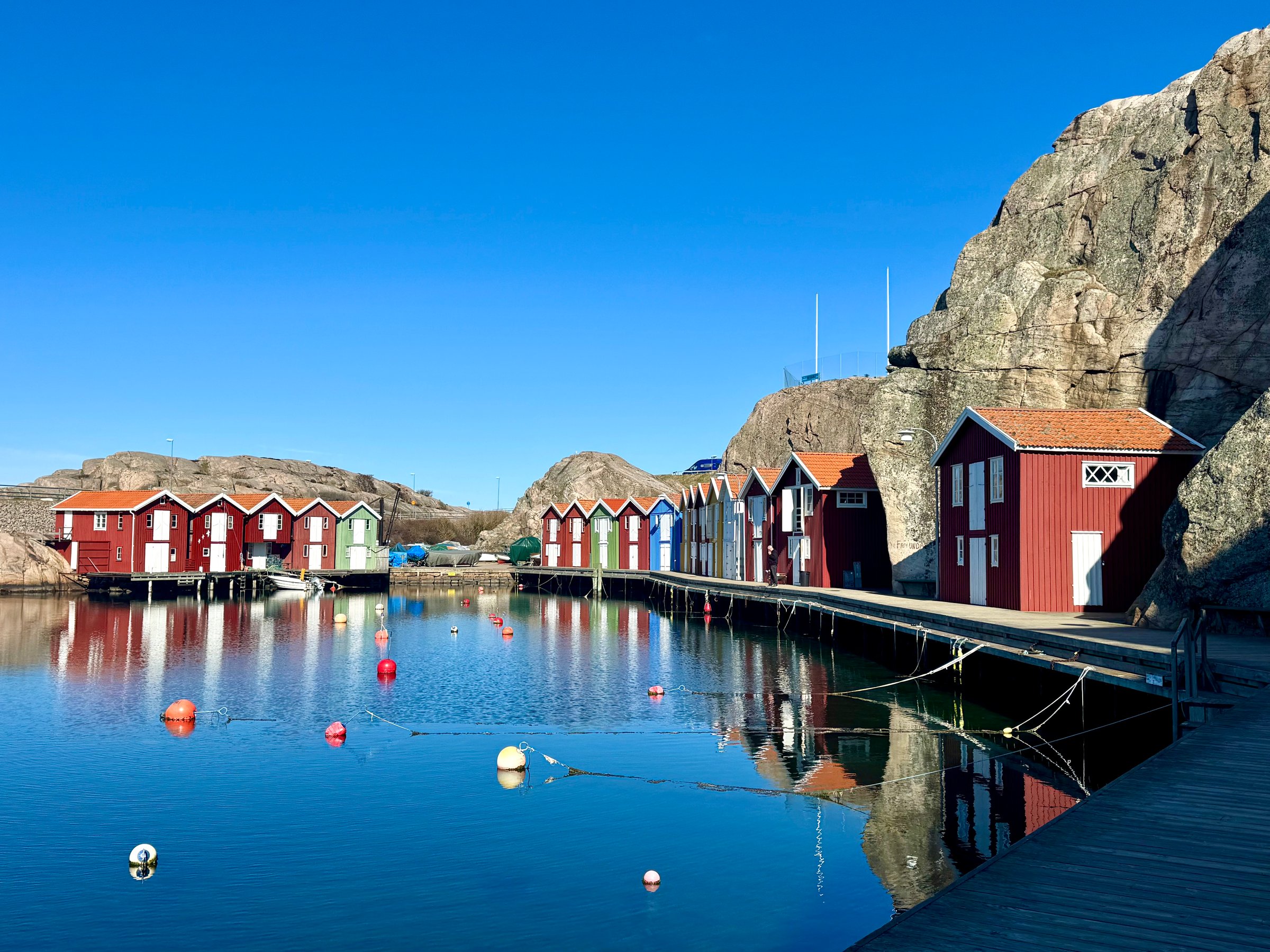 Colorful boathouses in Smögen. Fisherman's huts. Panoramic view of colorful wooden houses along the rocky cliff on the sea channel shore in the old fishing harbor on a sunny day, Sweden.