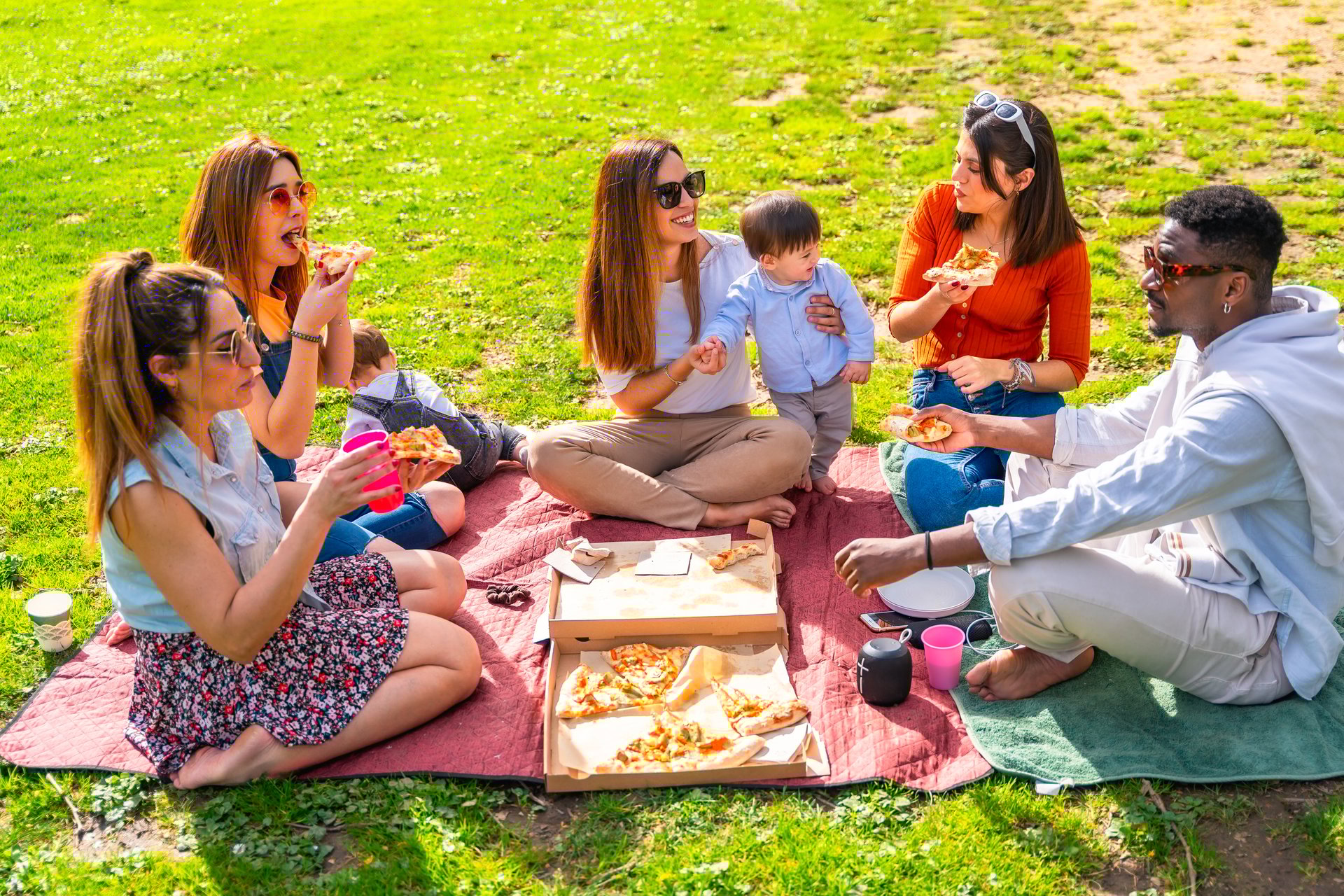 Friends and family enjoying a sunny day at the park, sharing pizza and good times together