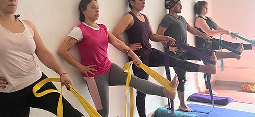 Group of people practicing yoga with resistance bands against a wall, each extending one leg forward.