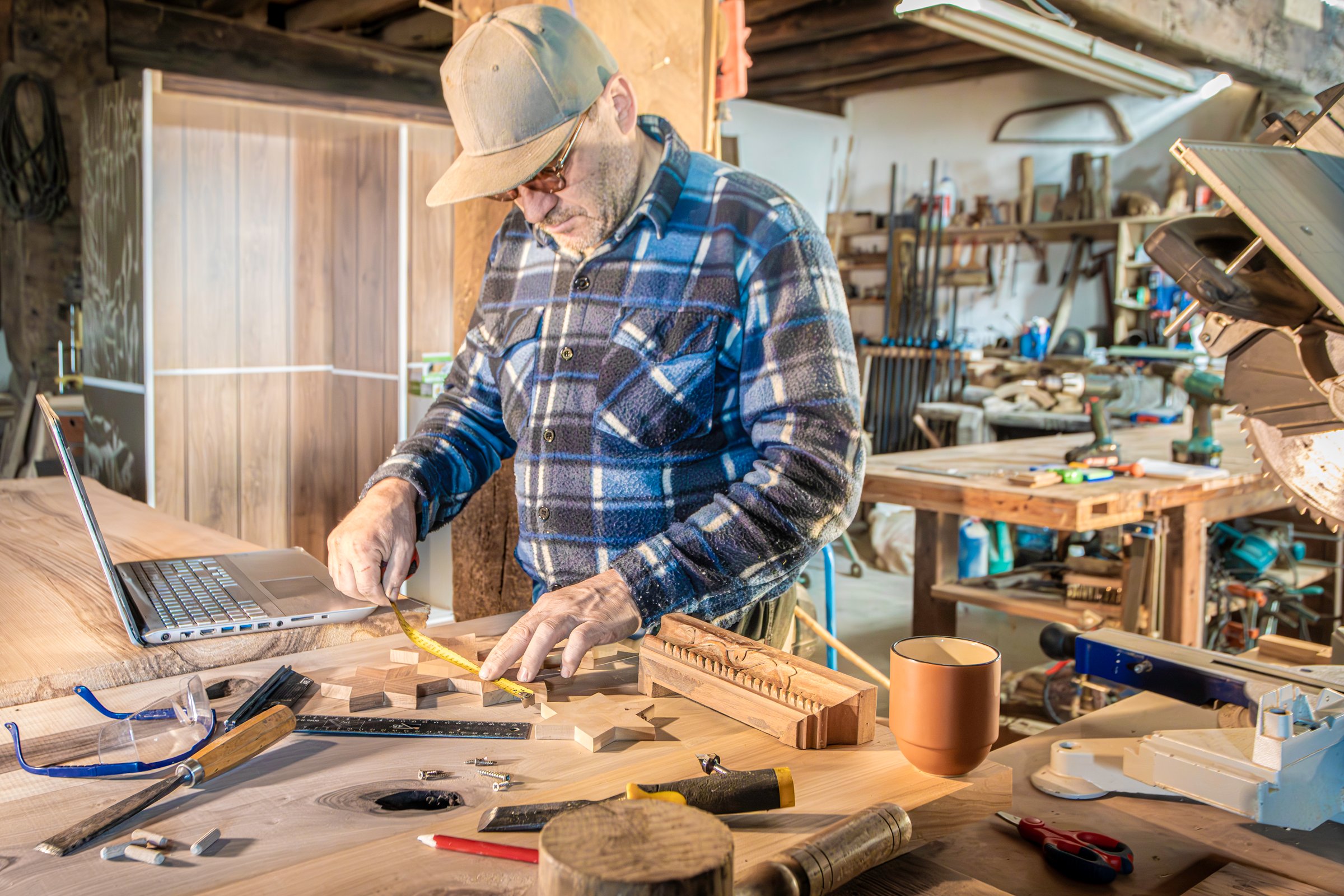 carpenter and measuring wood pieces for joinery with laptop computer and professional carpentry tools
