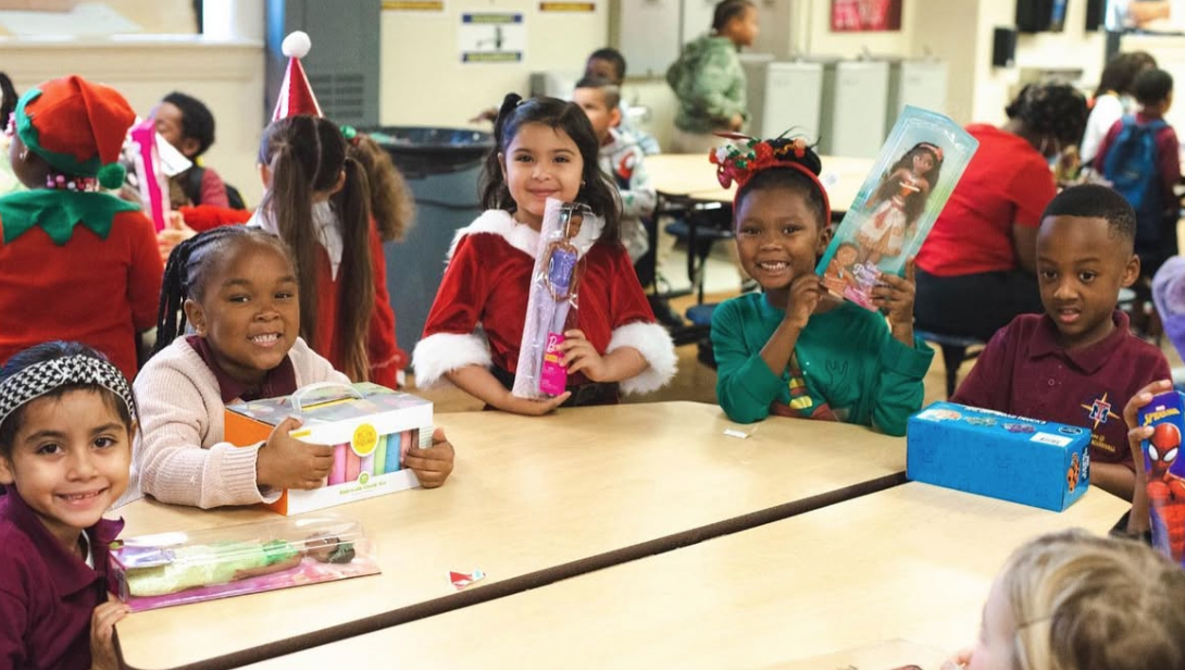 Children at a table holding toys, smiling, and wearing festive attire in a classroom setting.