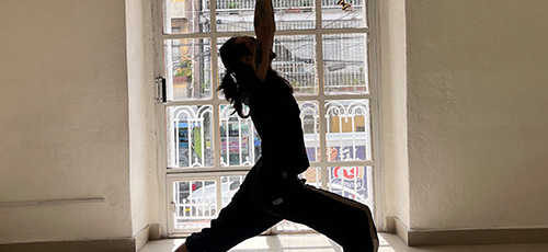 Person practicing yoga in warrior pose inside a room with a large window and natural light.