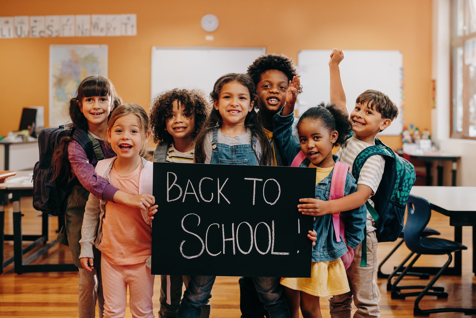 Back to school celebration. Excited elementary school class ready to learn on first day of class. Group of children smiling at the camera while holding a back to school sign in a classroom.