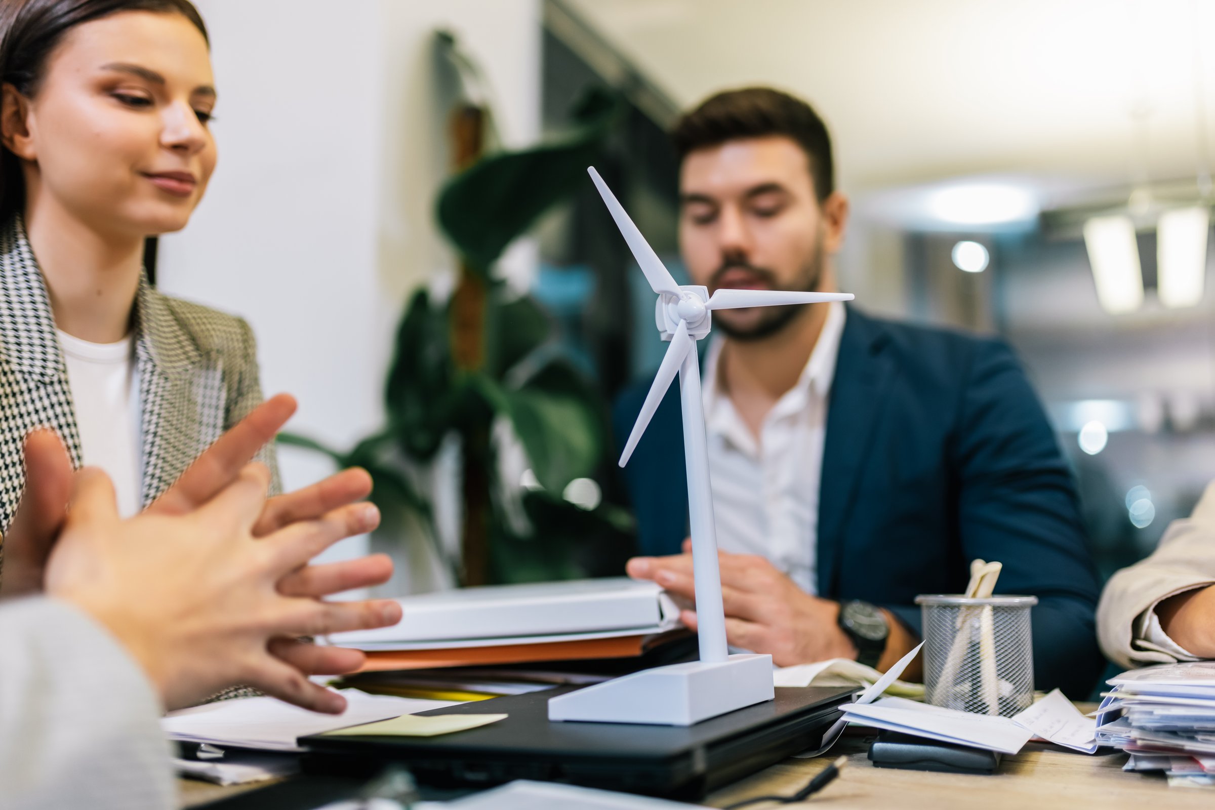 Bbusiness people talking about sustainable energy. They have windmill on a table and they are doing work on a laptop.