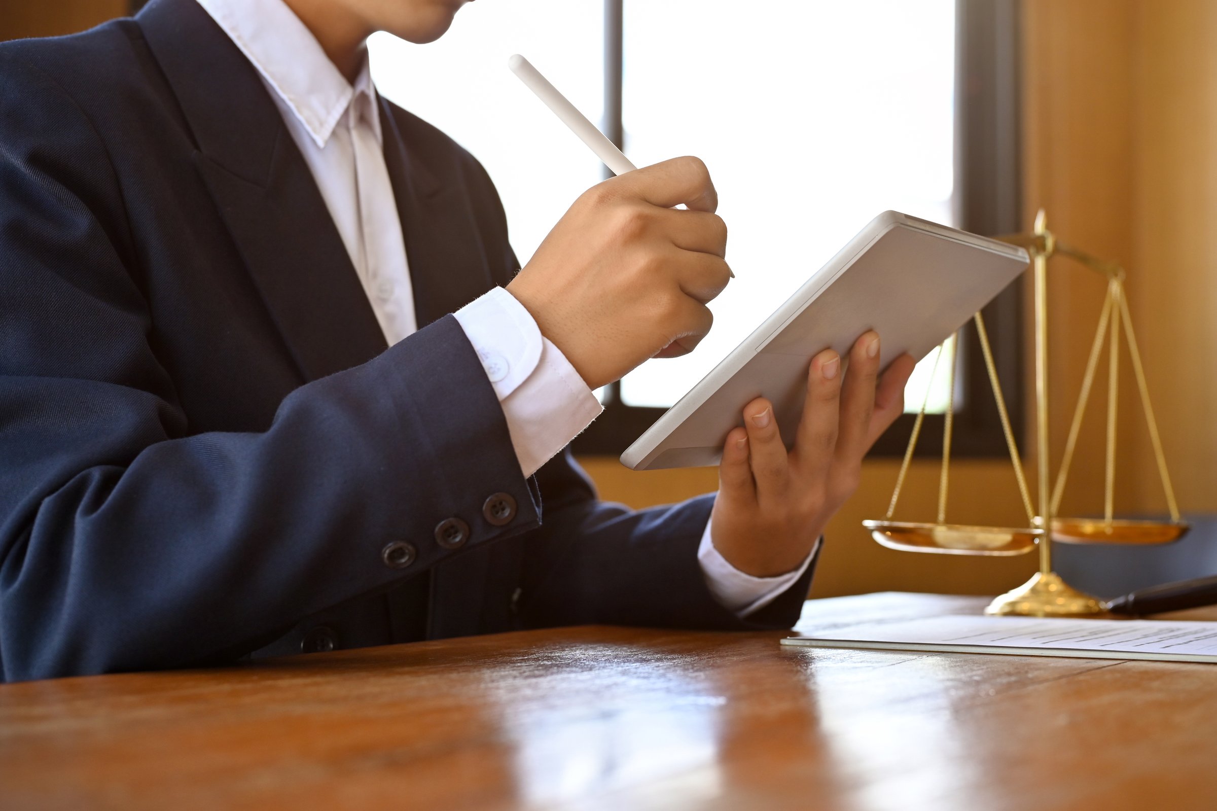 Professional Asian male lawyer or attorney at his office desk, using a digital tablet touchpad to check his work schedule. cropped image