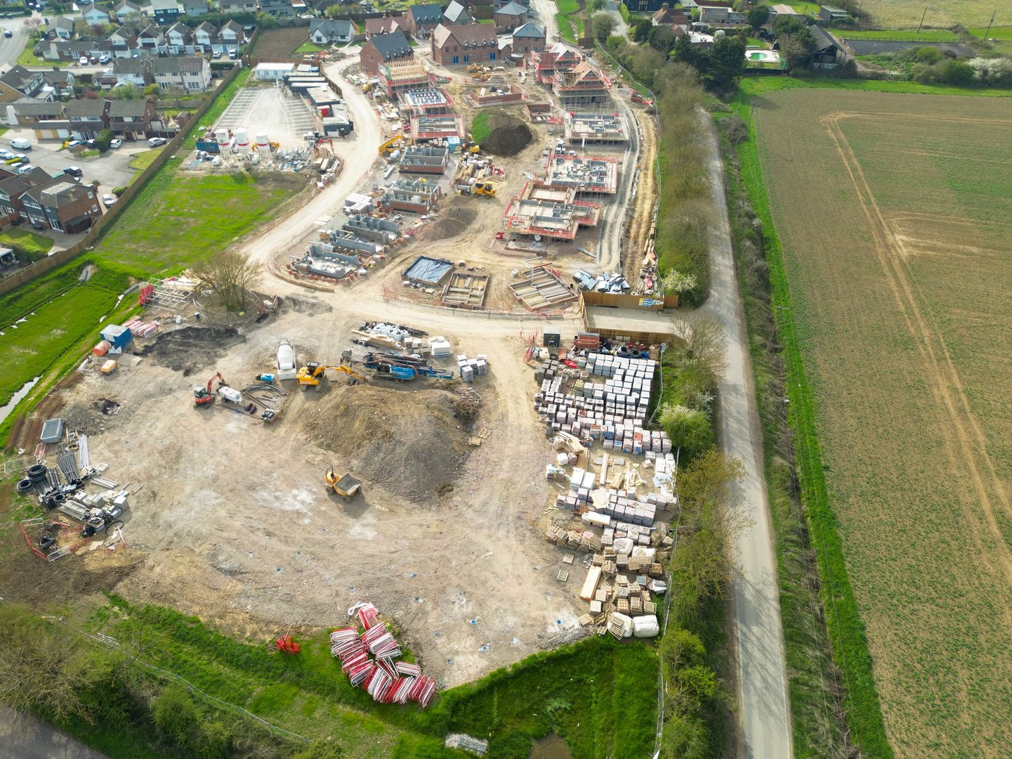 Drone high altitude view of an expansive new housing development project in rural East Anglia. Homes seen in various stages of construction, the old village is on the left.