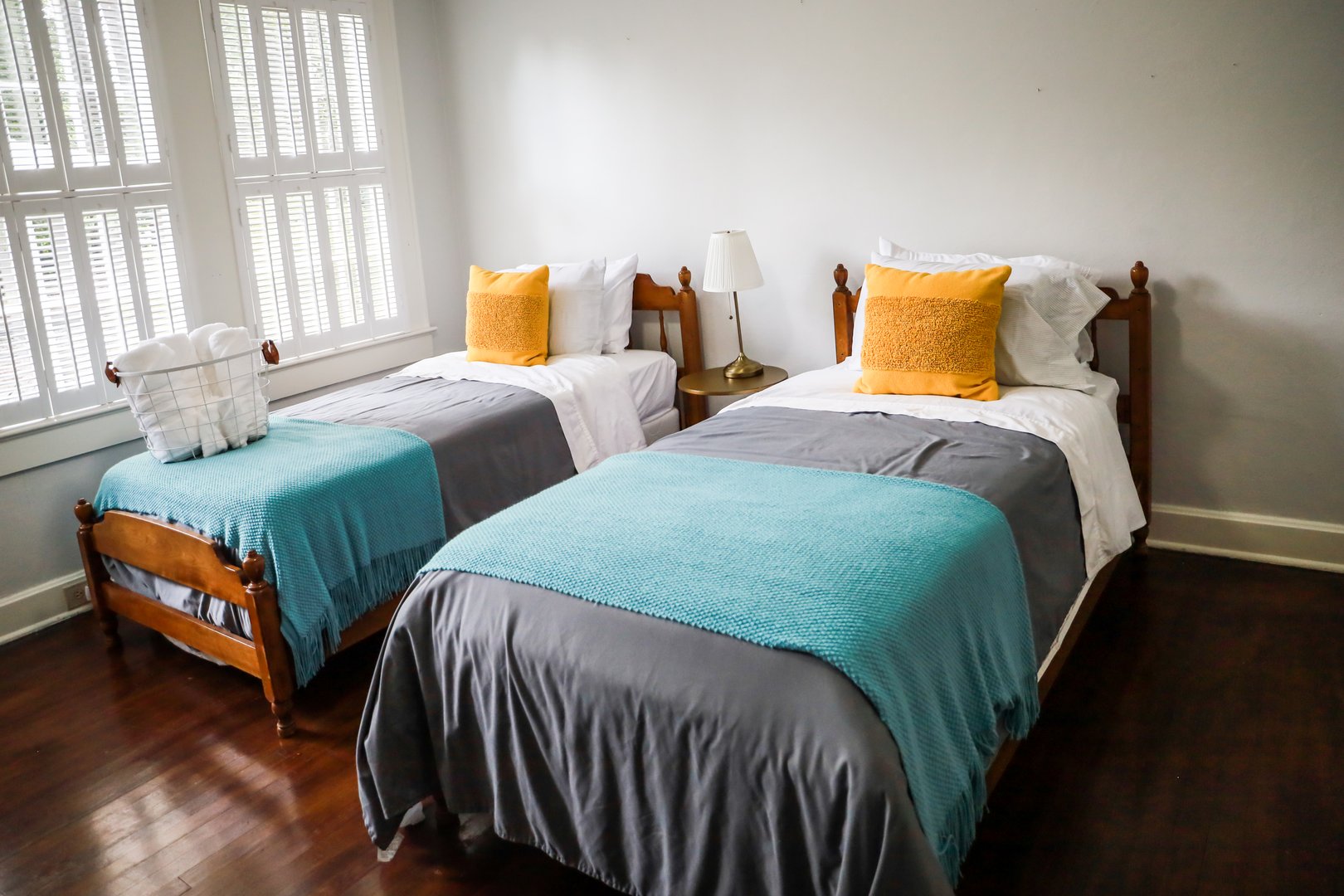 A guest bedroom with two twin beds with turquoise and gray bedspreads and yellow decorative pillows.