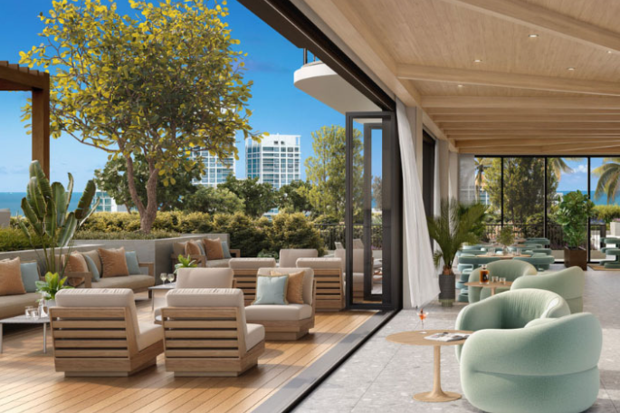 Modern outdoor seating area with wooden furniture, plush chairs, and ocean view, blending indoor and outdoor spaces.