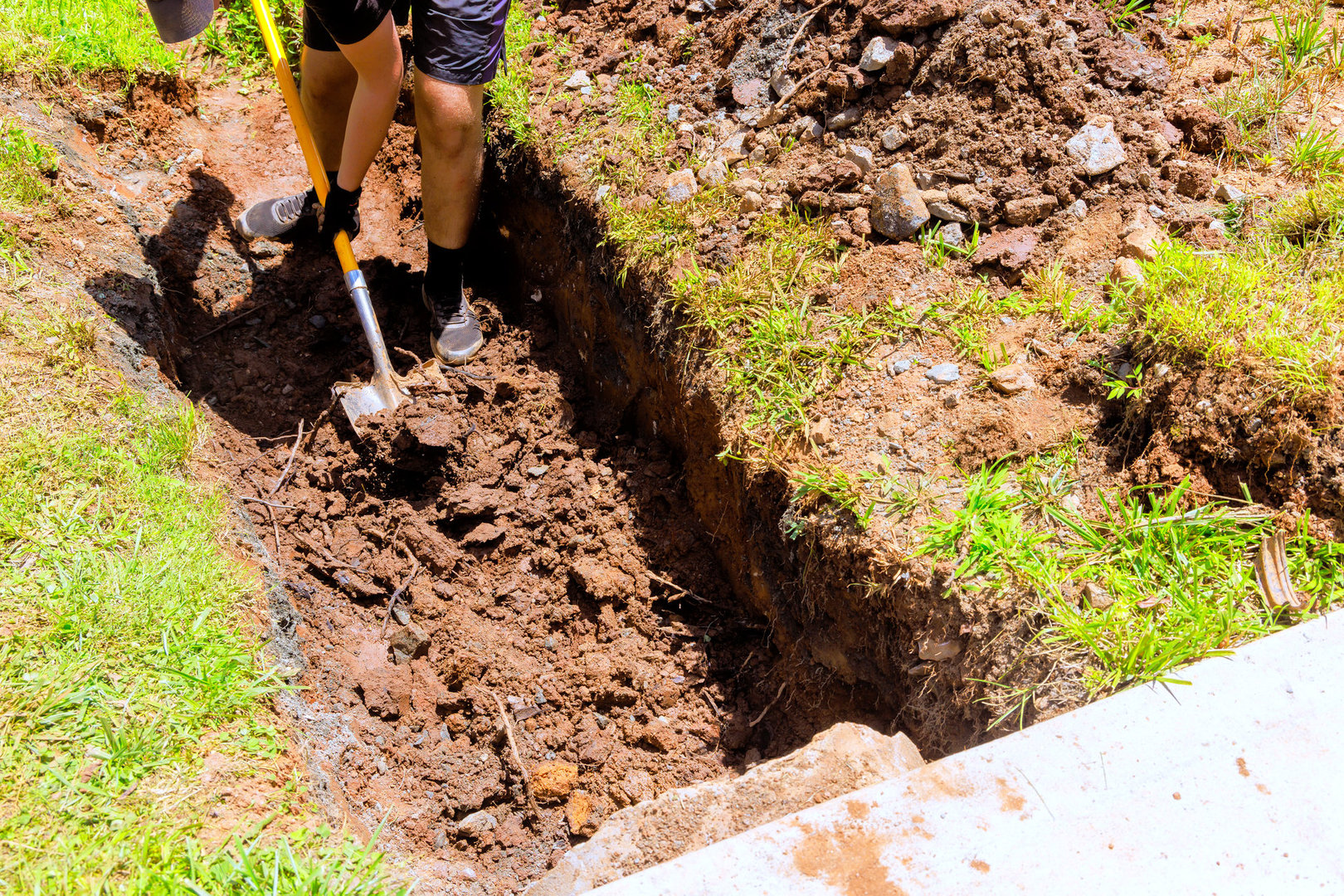 Worker digging trench with shovel for drainage pipe