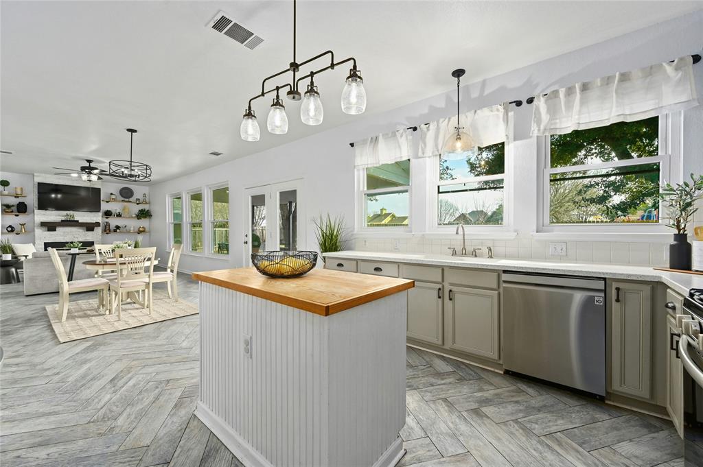 Modern kitchen with a central island, hanging lights, white cabinets, and stainless steel appliances. Dining area in the background.