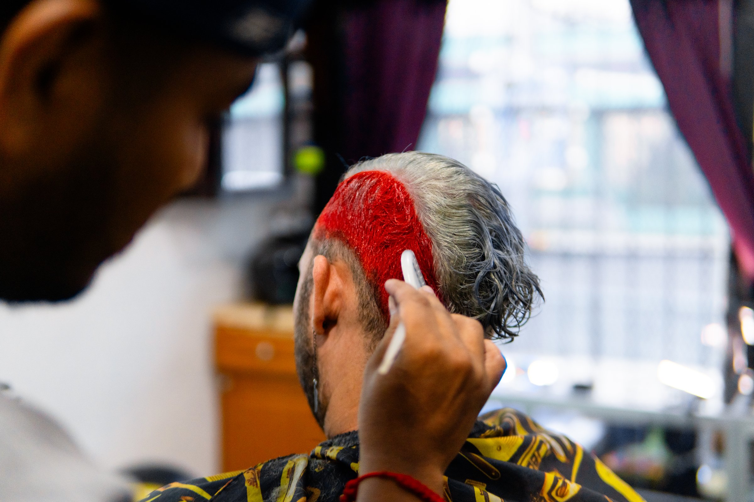 Hairdresser coloring the hair of a customer with red dye in a barbershop