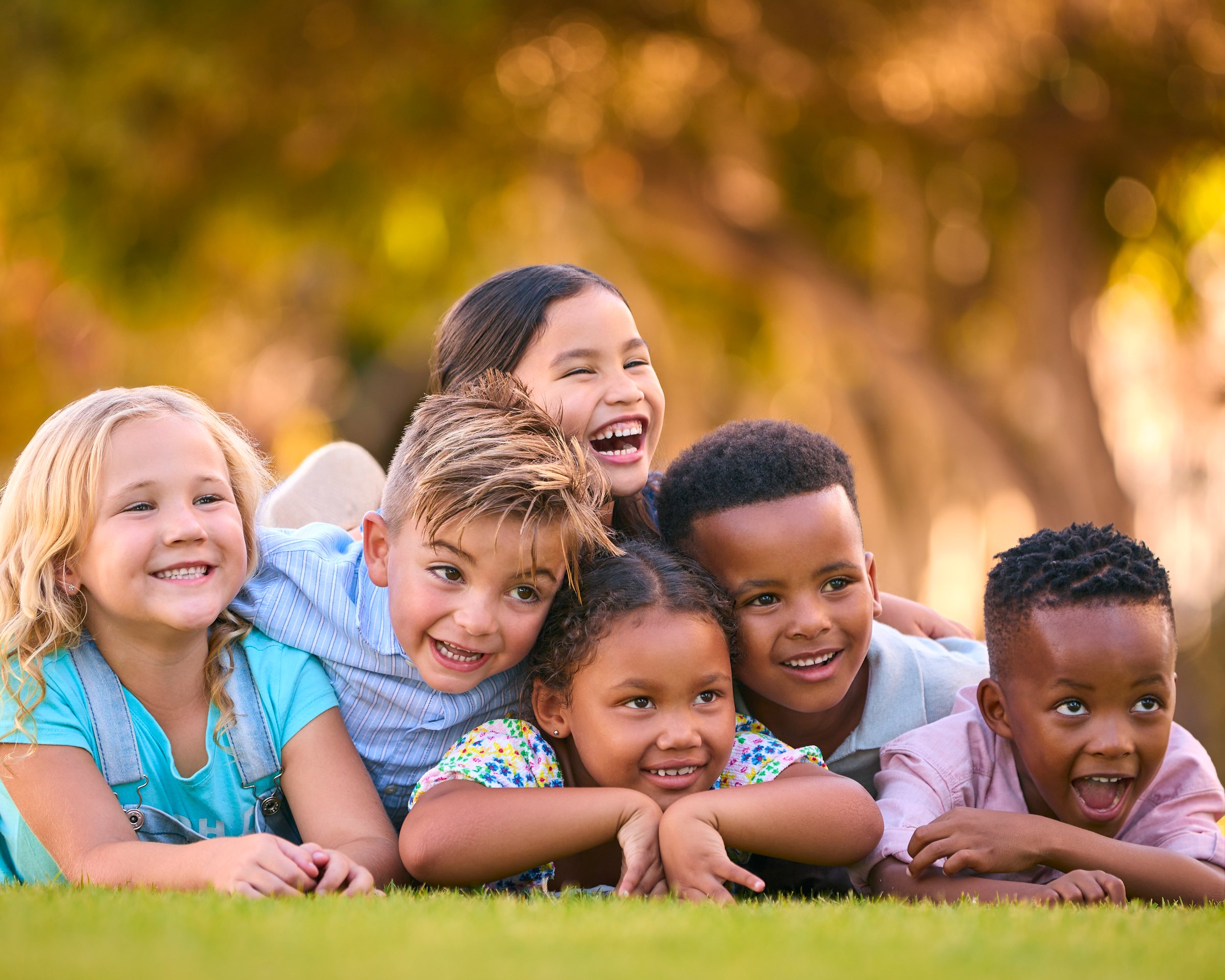 Portrait Of Multi-Cultural Primary Or Elementary School Student Friends Lying On Grass Outdoors