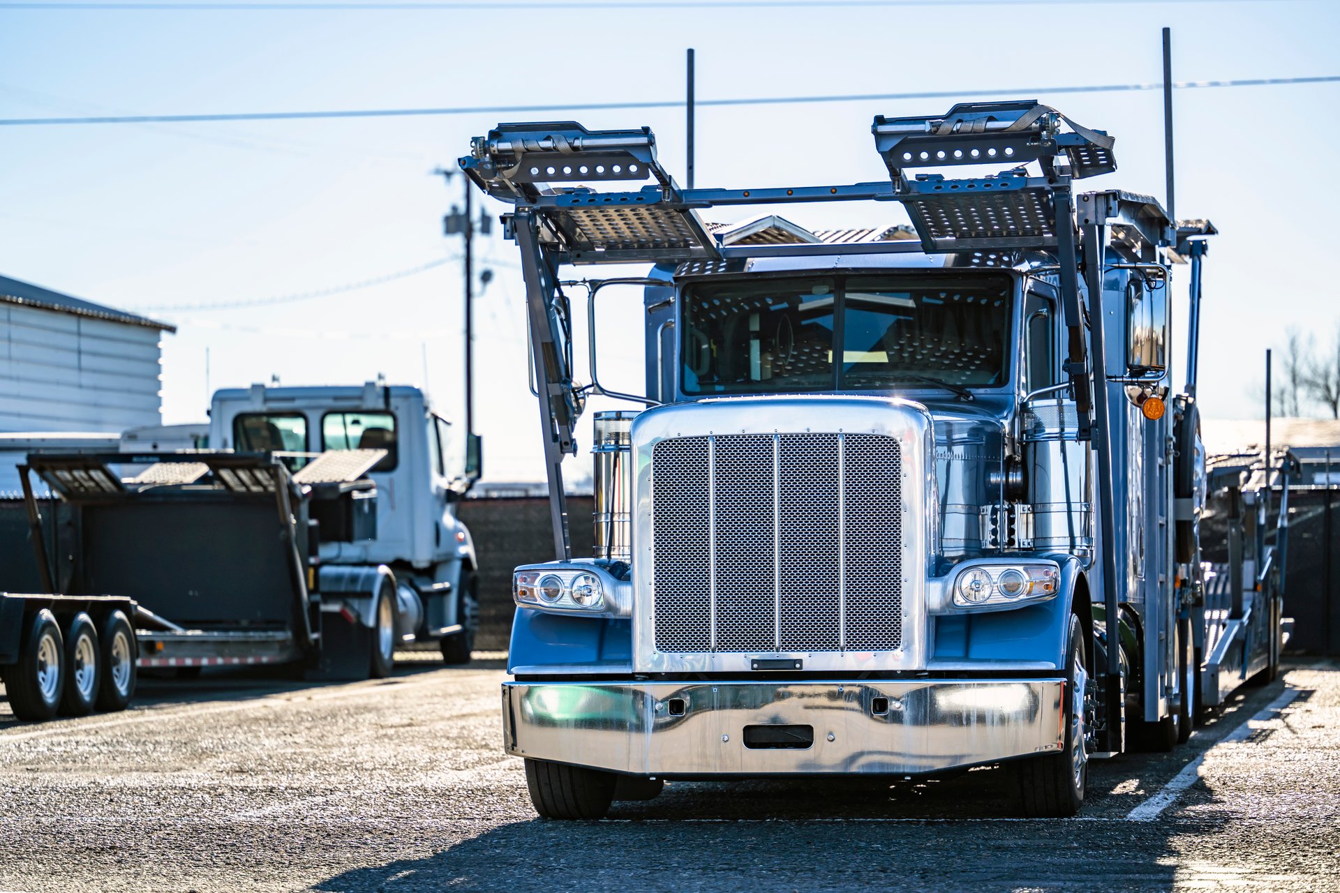 Industrial blue classic car hauler classic bonnet big rig semi truck with empty two level modular hydraulic semi trailer standing on the warehouse industrial parking lot waiting for the next load