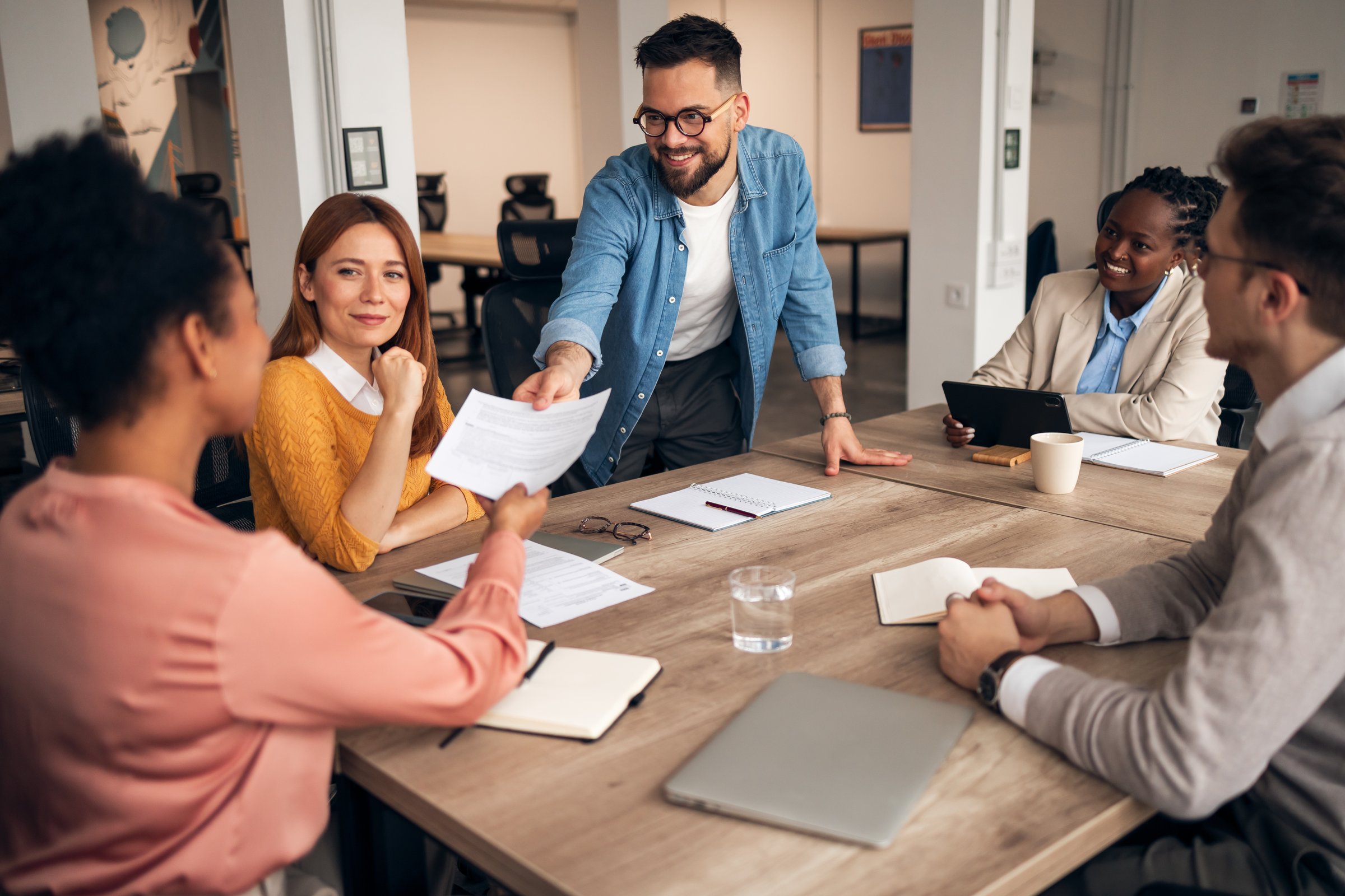 Group of professionals engaged in active discussion and document sharing during a business meeting in a modern office.