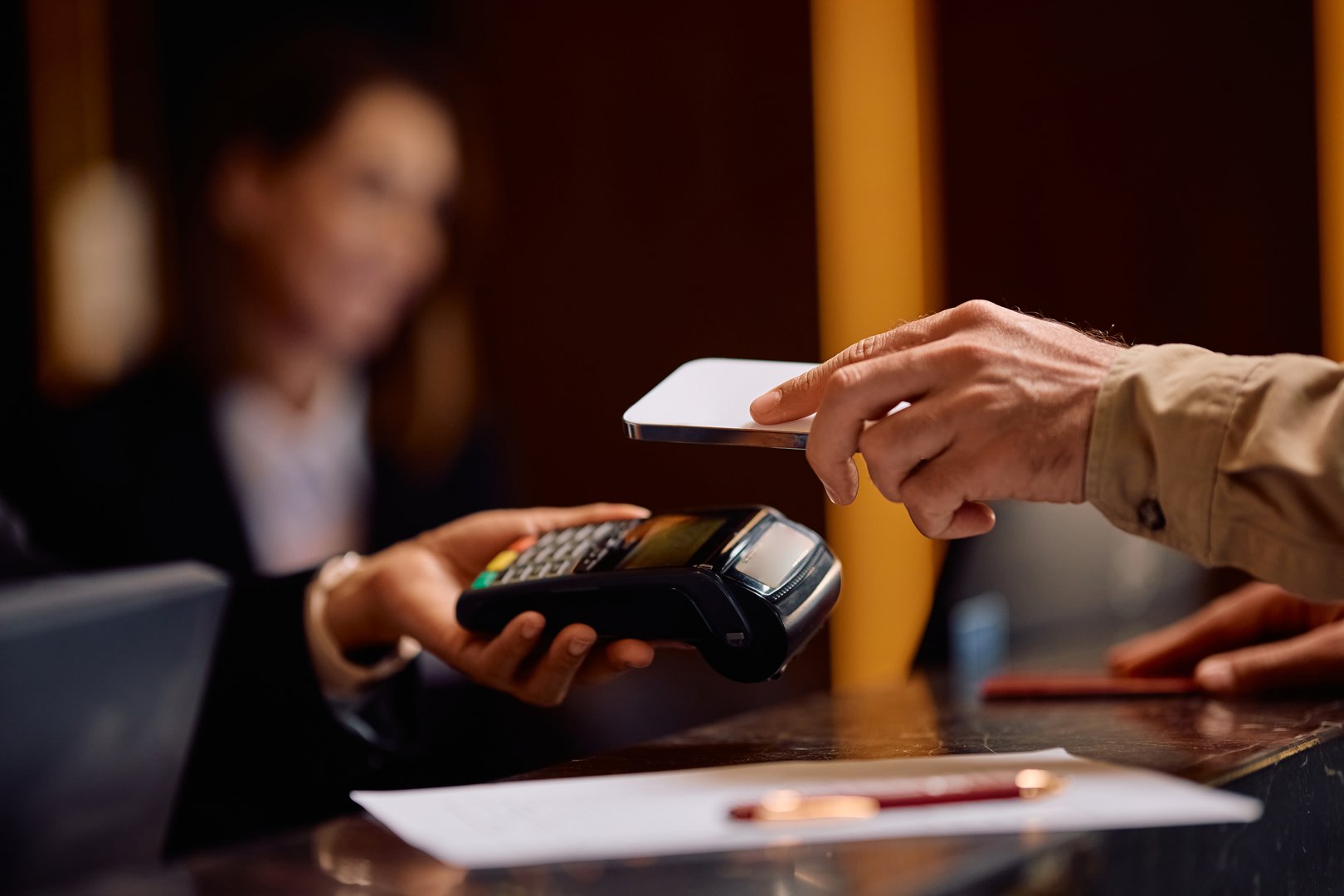 Close up of guest using smart phone while paying for his stay at the hotel.