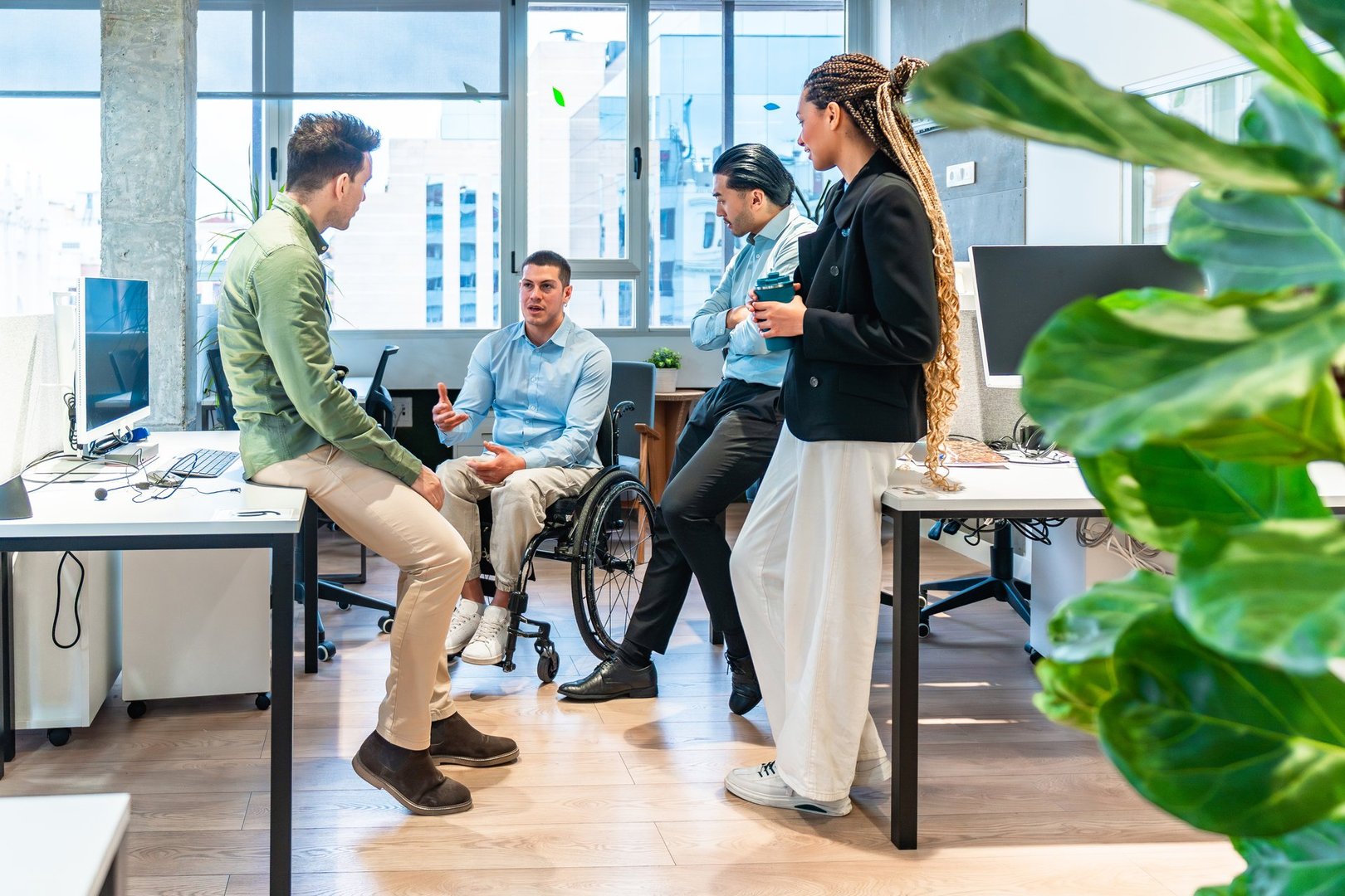 Four business colleagues engaging in a productive discussion in a contemporary office setting, demonstrating inclusion and teamwork with a disabled team member