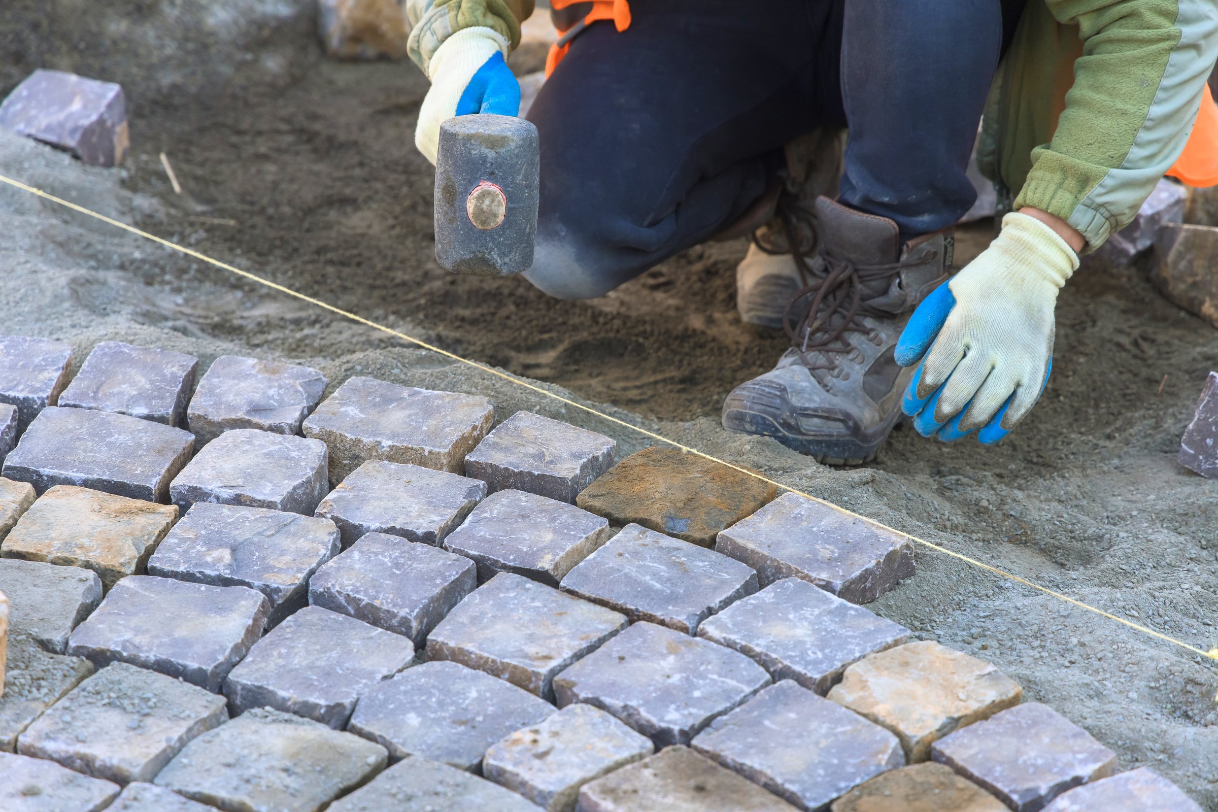Laborer carefully positions cobblestones while maintaining alignment in construction setting during works day hours