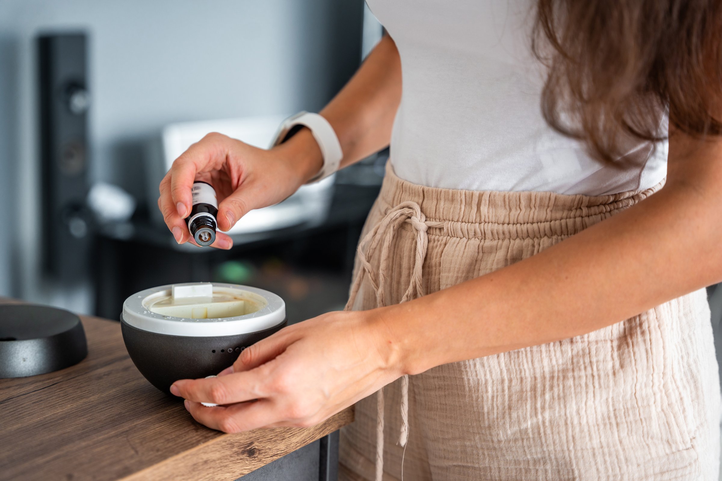 Woman adding oil to the grey aroma oil diffuser on light table at home, air freshener. High quality photo