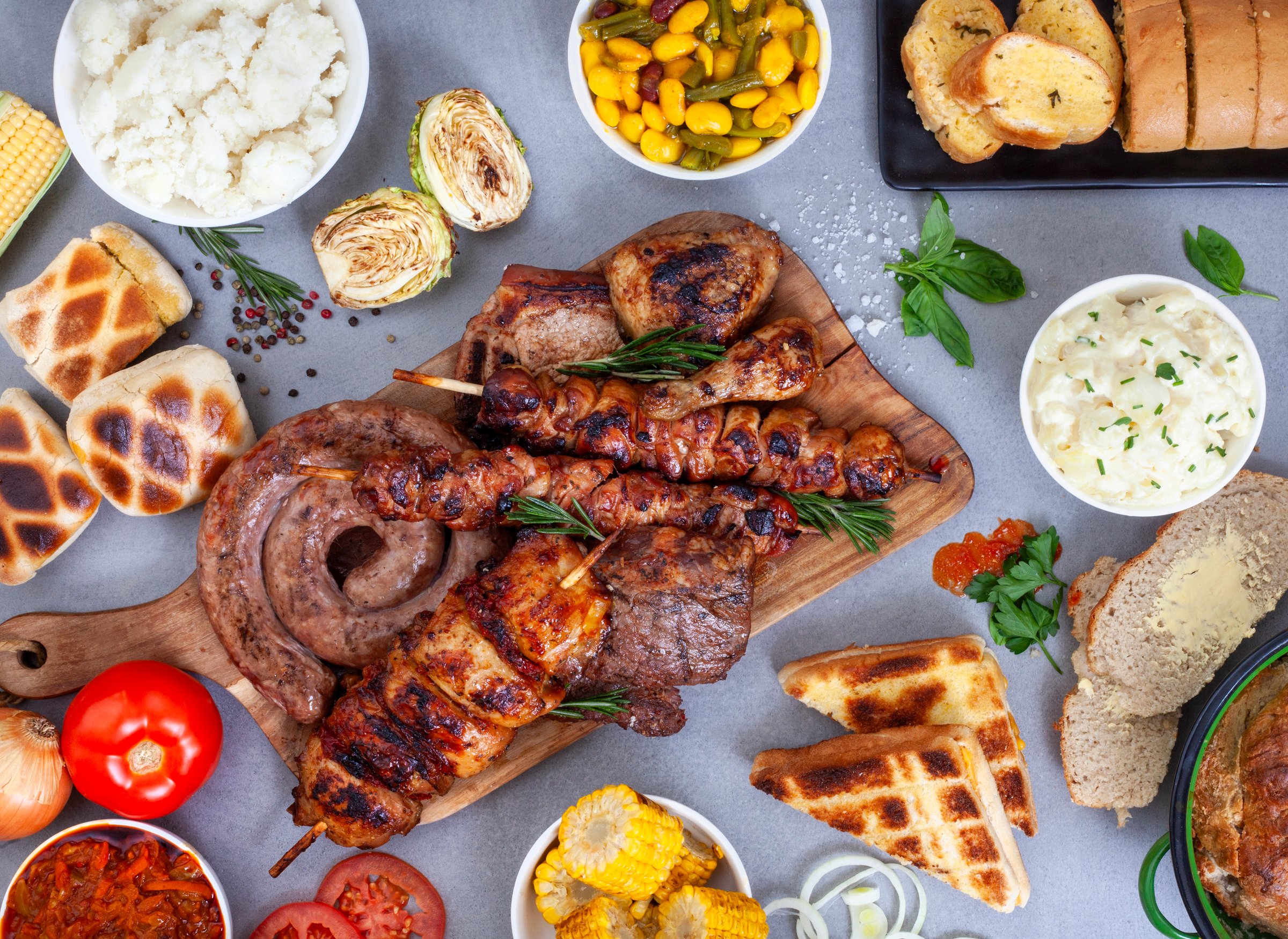flat lay of Traditional South African Braai meal on table, meat and sides on grey surface