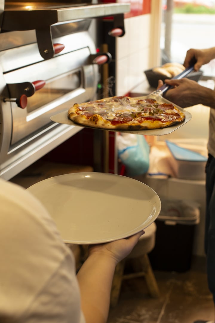 A delicious hot pizza is being carefully removed from the oven and placed on a plate for the eager diners waiting