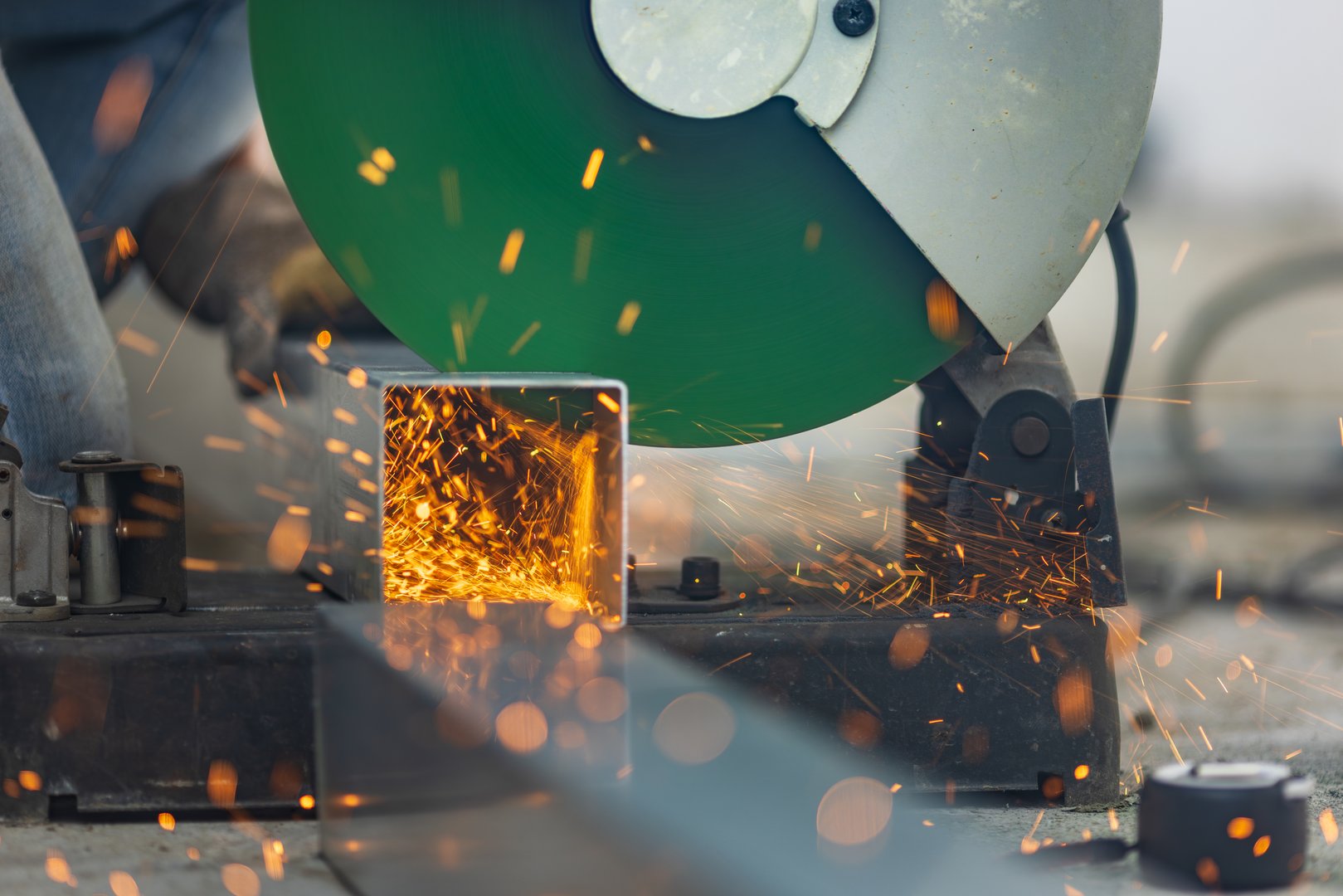 Worker cutting steel rectangular pipe in construction site.