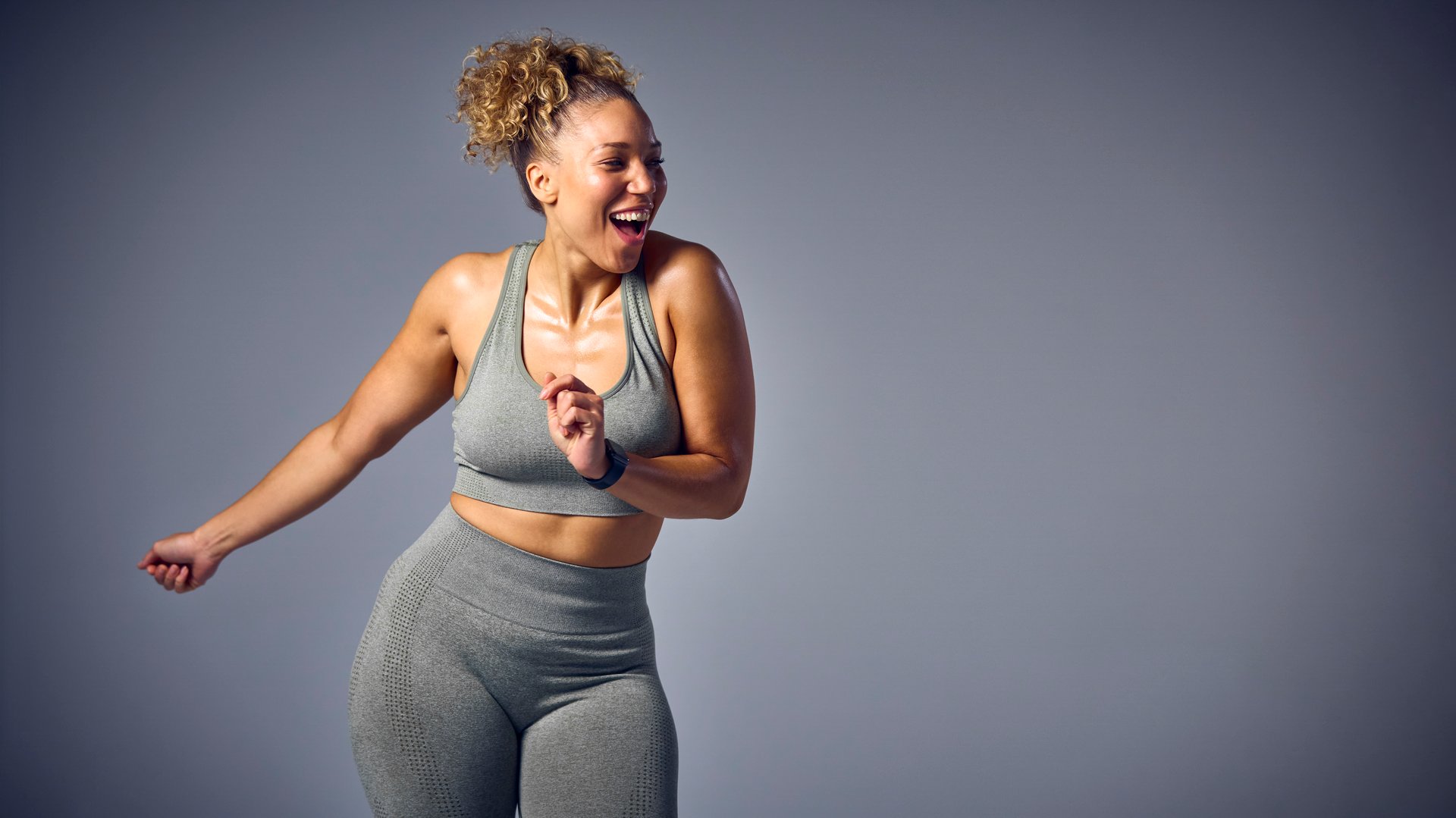 Studio Shot Of Woman Wearing Gym Fitness Clothing Dancing In Zumba Class On Grey Background