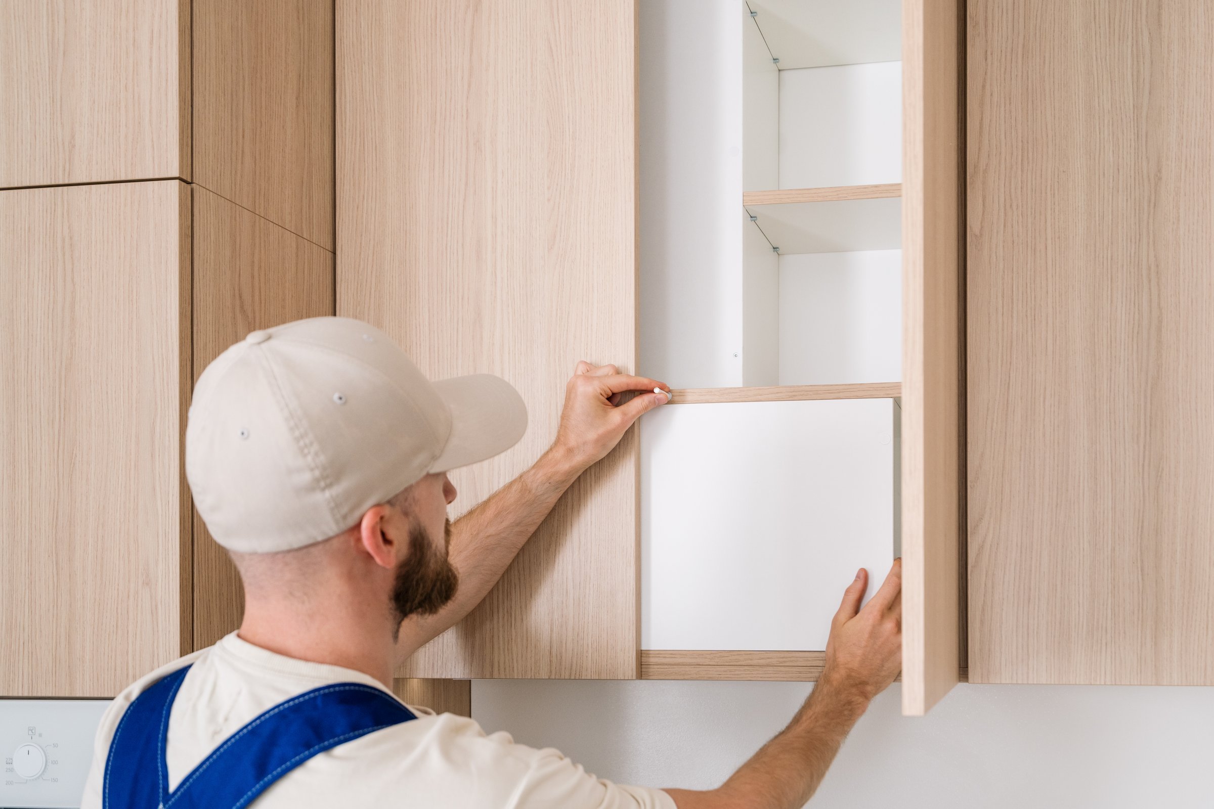 A professional handyman is working on installing new wooden cabinet with open door and adjusting mechanism of soft close damper. Process of renovated kitchen.