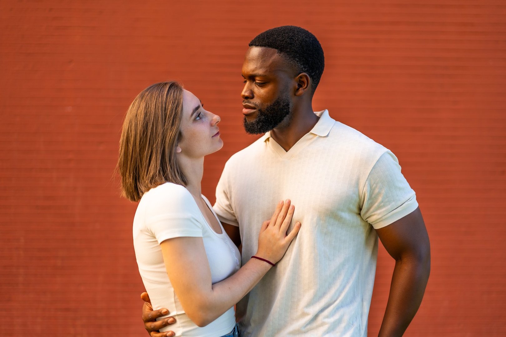 Mixed raced couple standing embracing and looking at each other against red brick wall