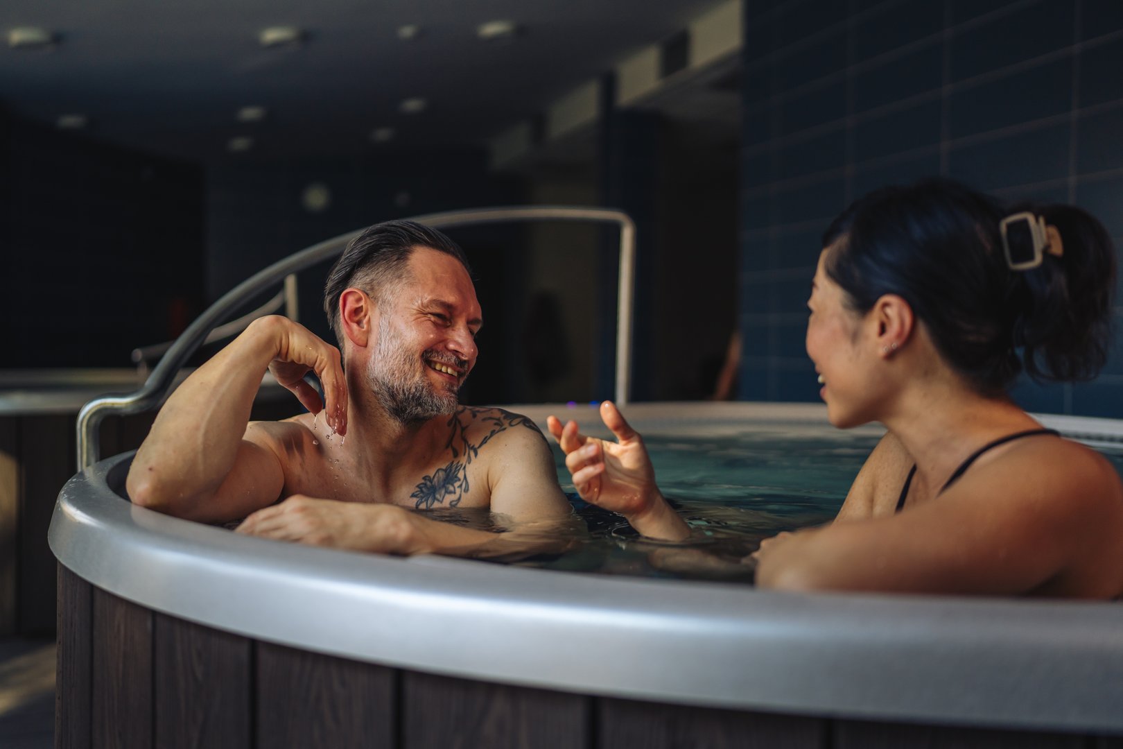Happy smiling couple relaxing in a warm hot tub at a luxury wellness resort, leaning on the spa edge and enjoying tranquil hydrotherapy, bonding and carefree vacation joy