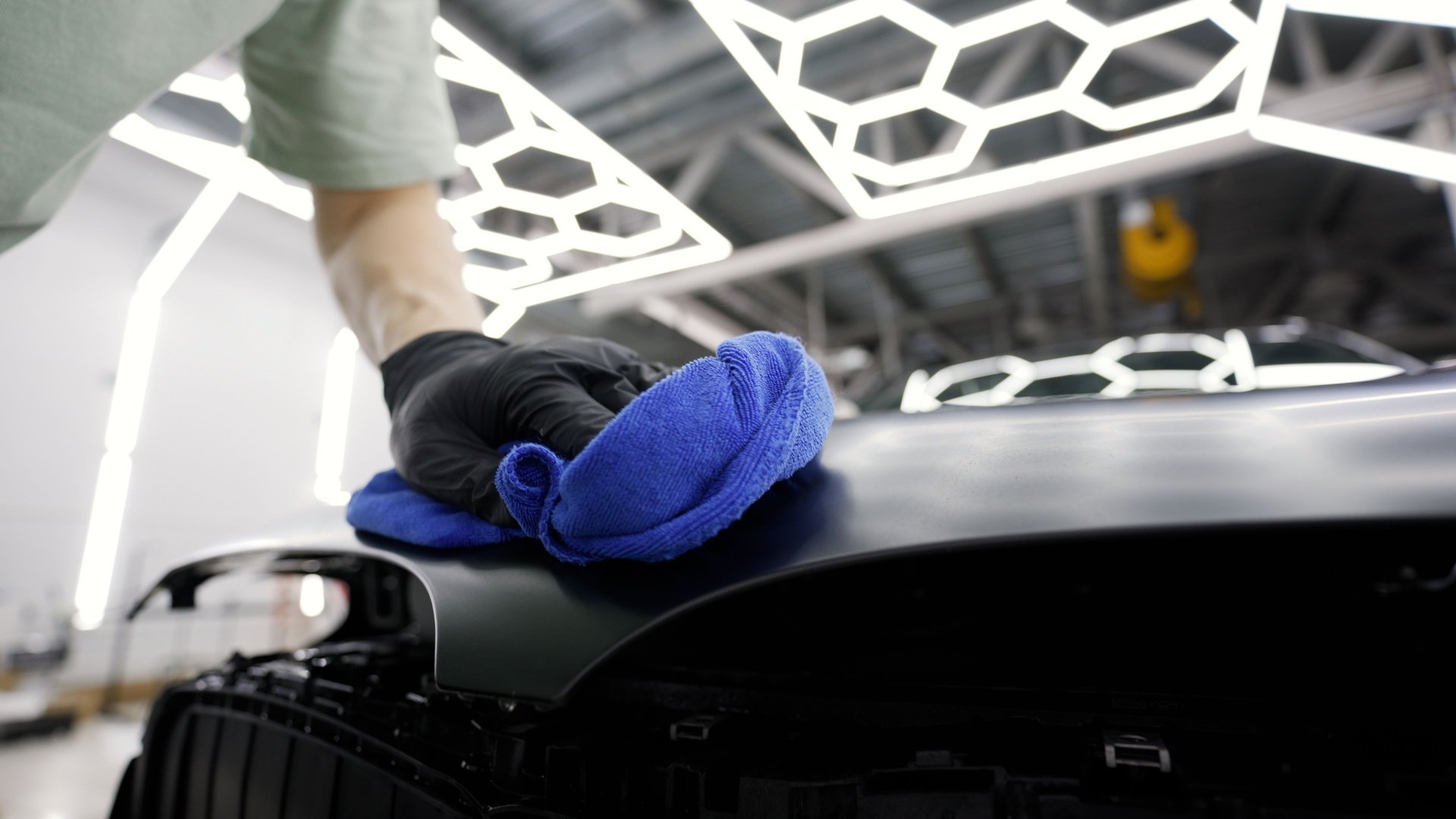 Professional car detailer using blue microfiber cloth, polishing hood of vehicle in auto shop, ensuring showroom finish