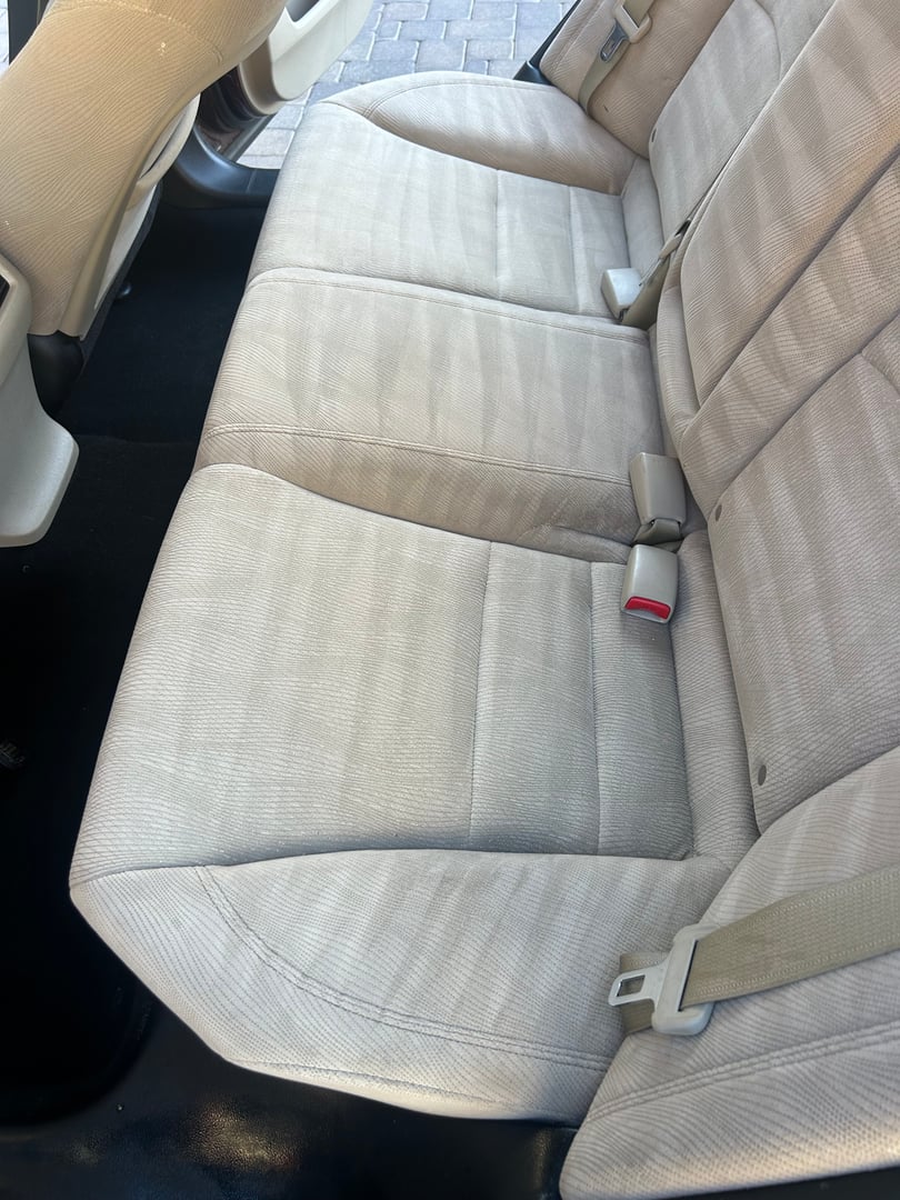 Interior of a car showing the clean beige fabric backseat with seatbelts and a glimpse of the floor and door trim.