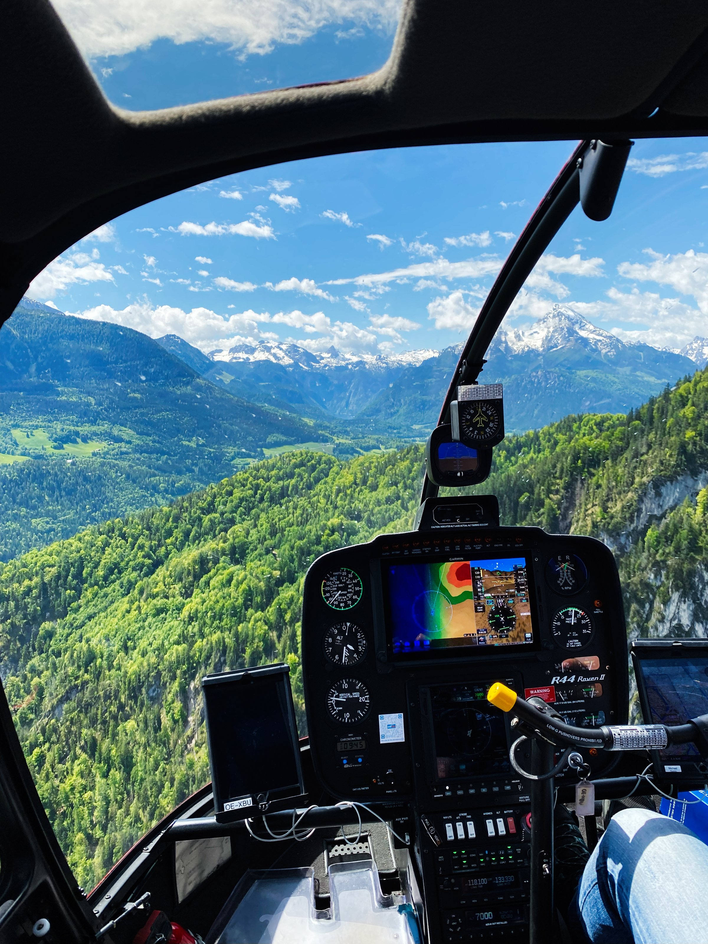 Gosau, Austria  - March 10, 2024: View from Robinson R44 Raven II helicopter cockpit showcasing an expansive green valley and mountains.