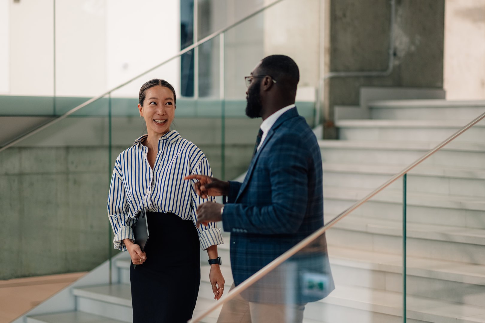 Two businesspeople walking down stairs, engaging in conversation within a modern office building, highlight collaboration and teamwork