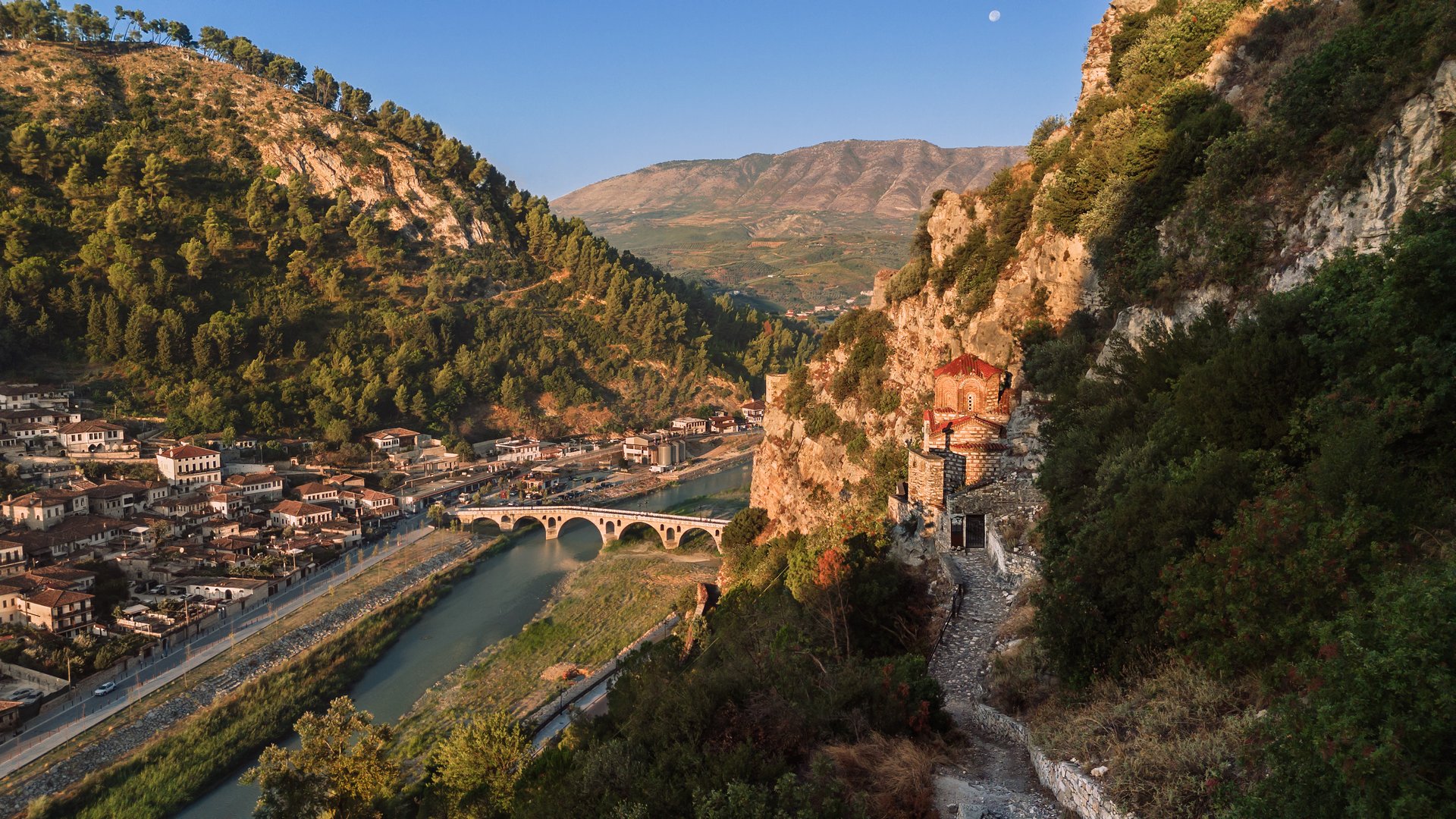 Early morning scene of Berat, Albania. Panoramic city drone landscape with traditional houses, Gorica bridge across Osum river, and medieval Byzantine Church of St. Michael carver in rock on hillside.