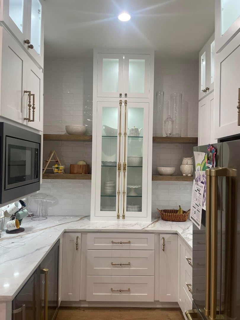 Modern kitchen with white cabinets, glass-front upper cabinets, and a marble countertop, featuring stainless steel appliances.