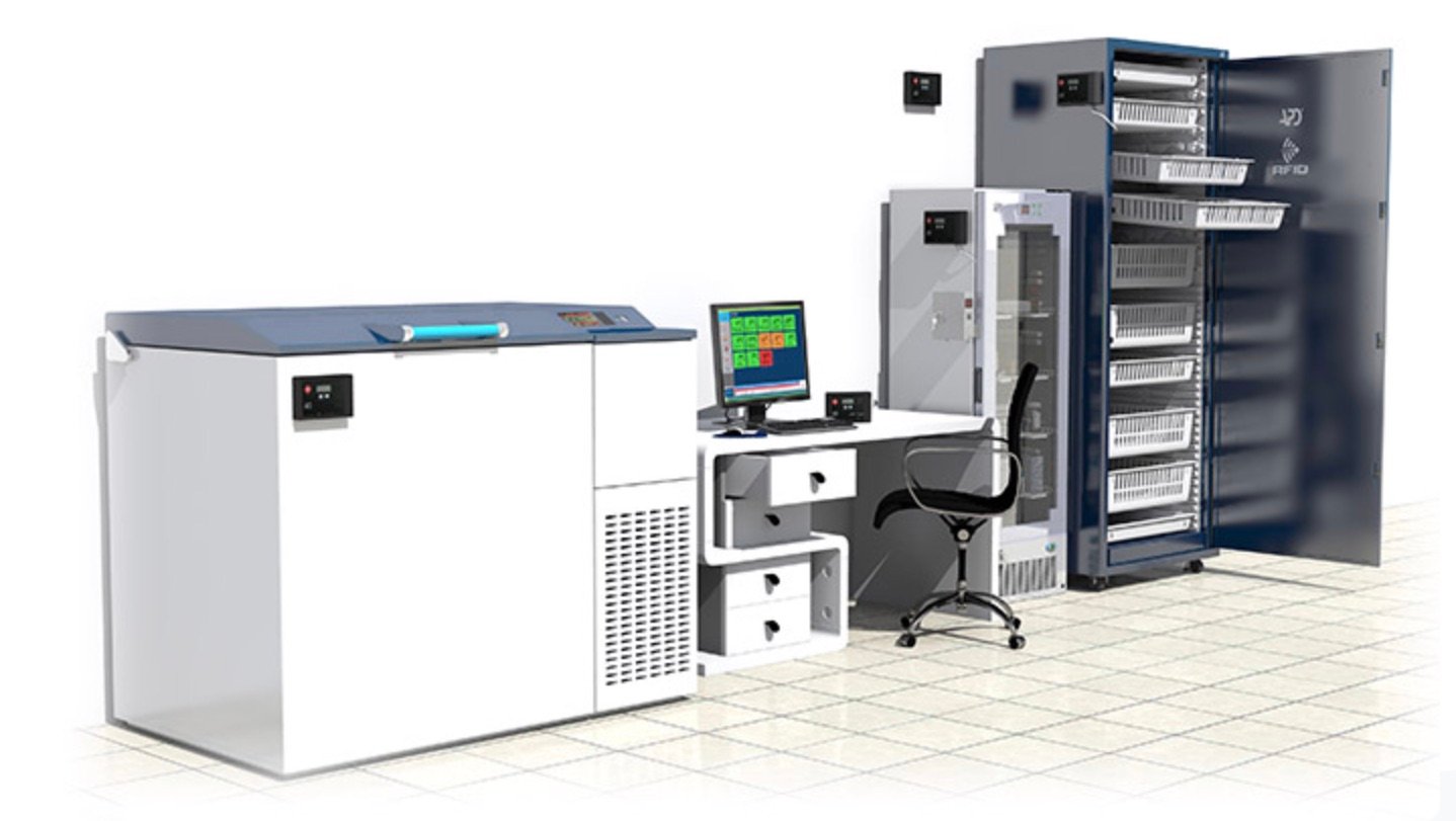 A modern laboratory setup with a computer, chair, and three large equipment units for storing samples, on a tiled floor.