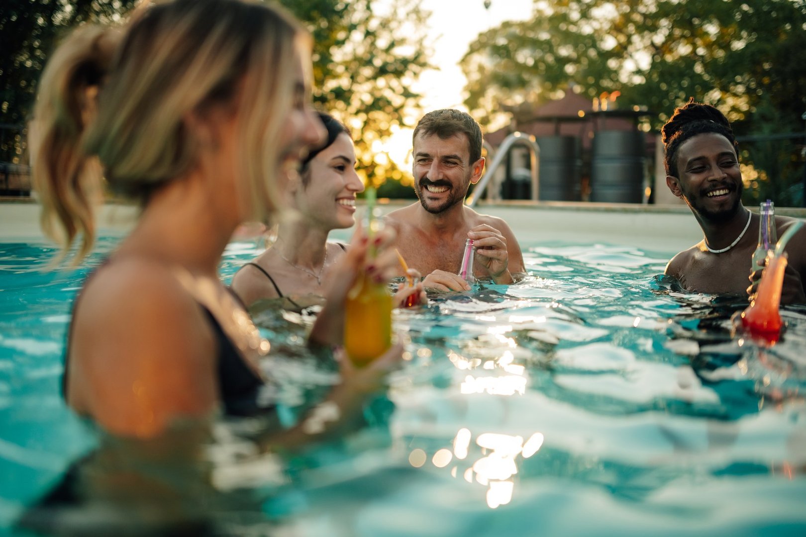 Cheerful friends are having fun and drinking cocktails in a swimming pool during a summer sunset party