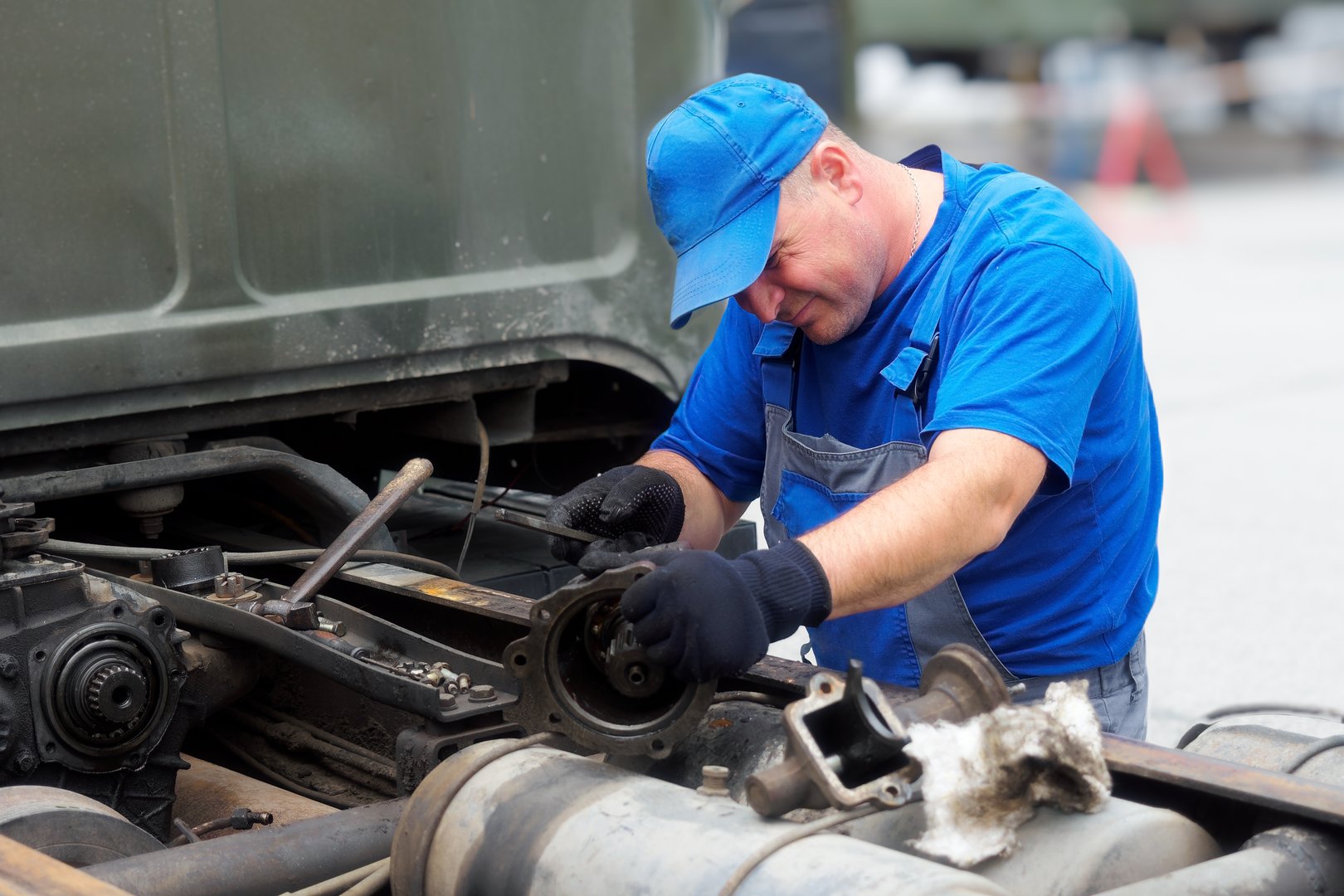 Mechanic in overalls repairs truck on summer day outside. Urgent repair of trucks. Authentic workflow..