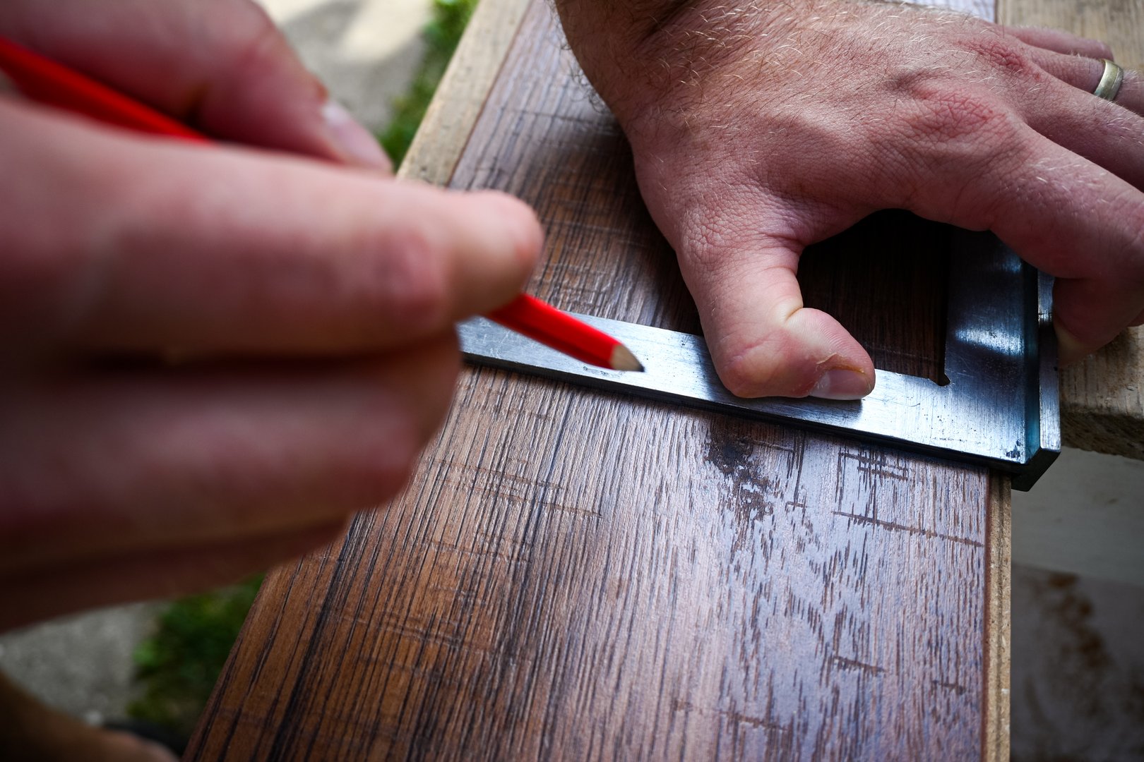 Construction worker using a carpenter square to mark a wooden plank with a pencil.