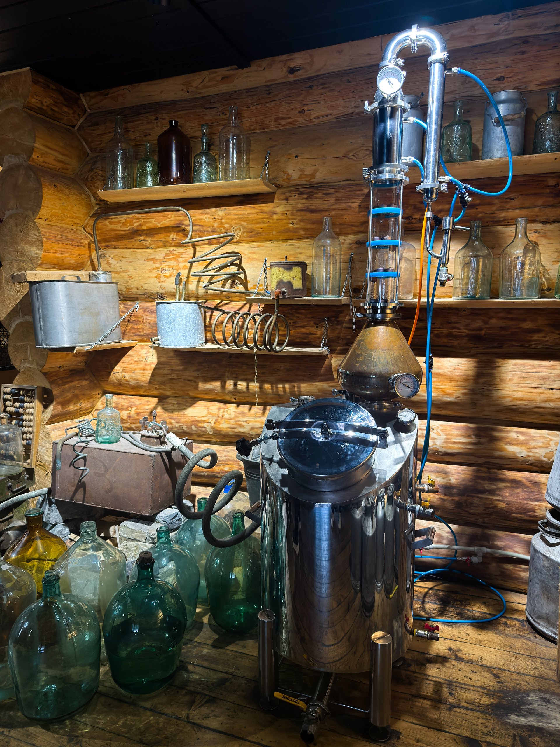 Rustic moonshine still in wooden cabin, artisan distiller workshop featuring copper alembic, stainless boiler