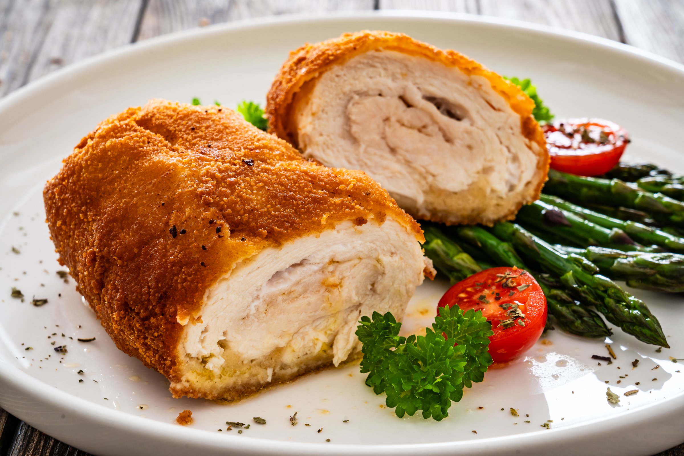 Cutlet de Volaille, wrapped chicken cutlet served with cooked green asparagus on wooden background